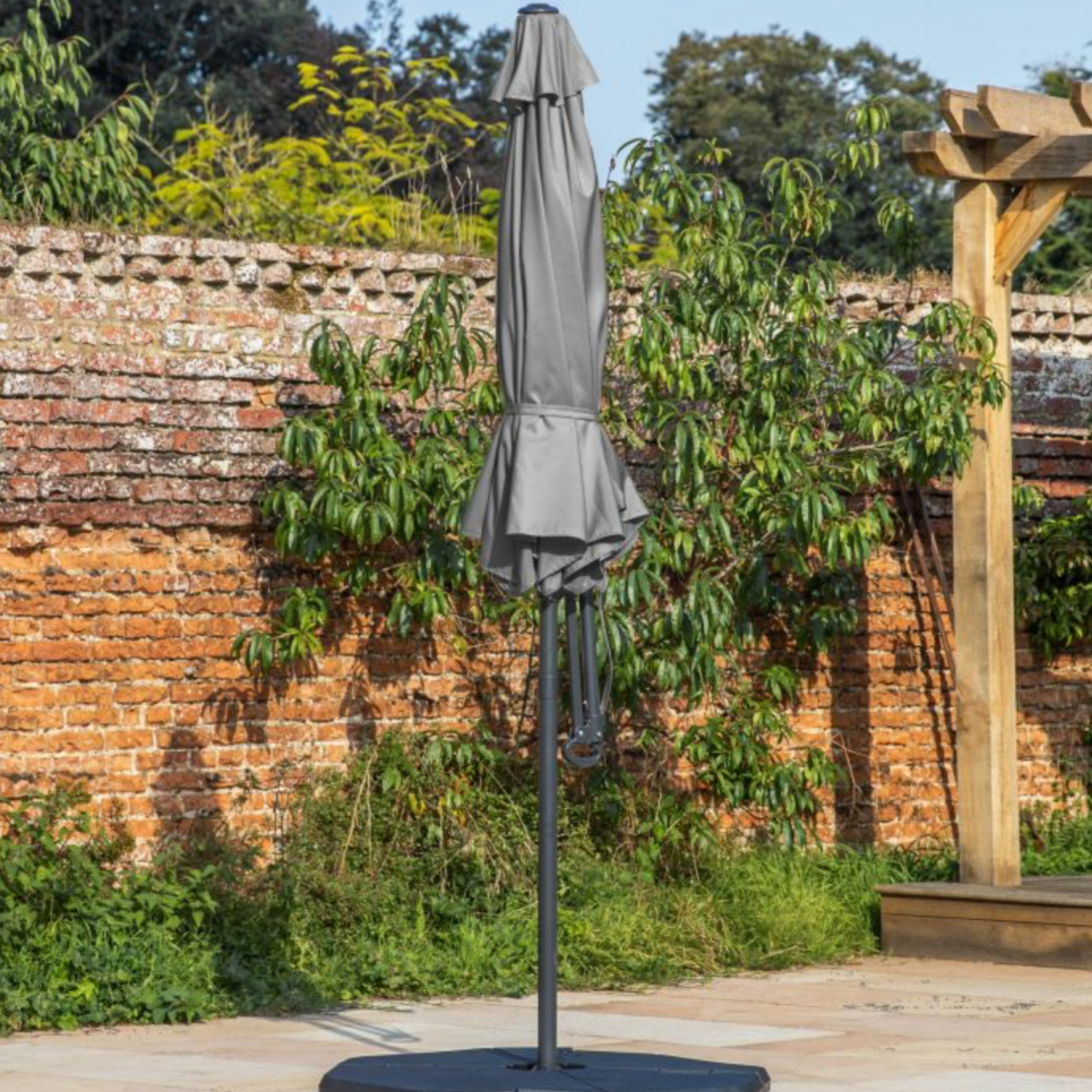 Garden umbrella with cover on a stand against a brick wall and greenery