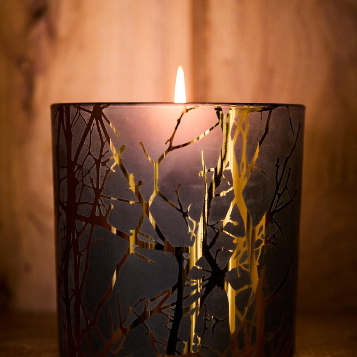 Lit candle holder in black and gold with wooden background