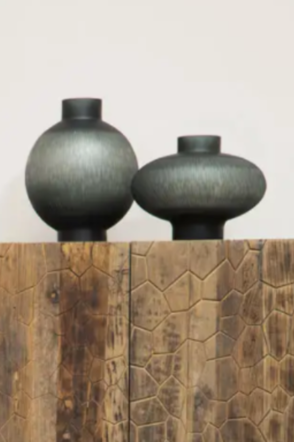 Squat grey cut glass vase and tall round vase in grey standing on a wooden plinth