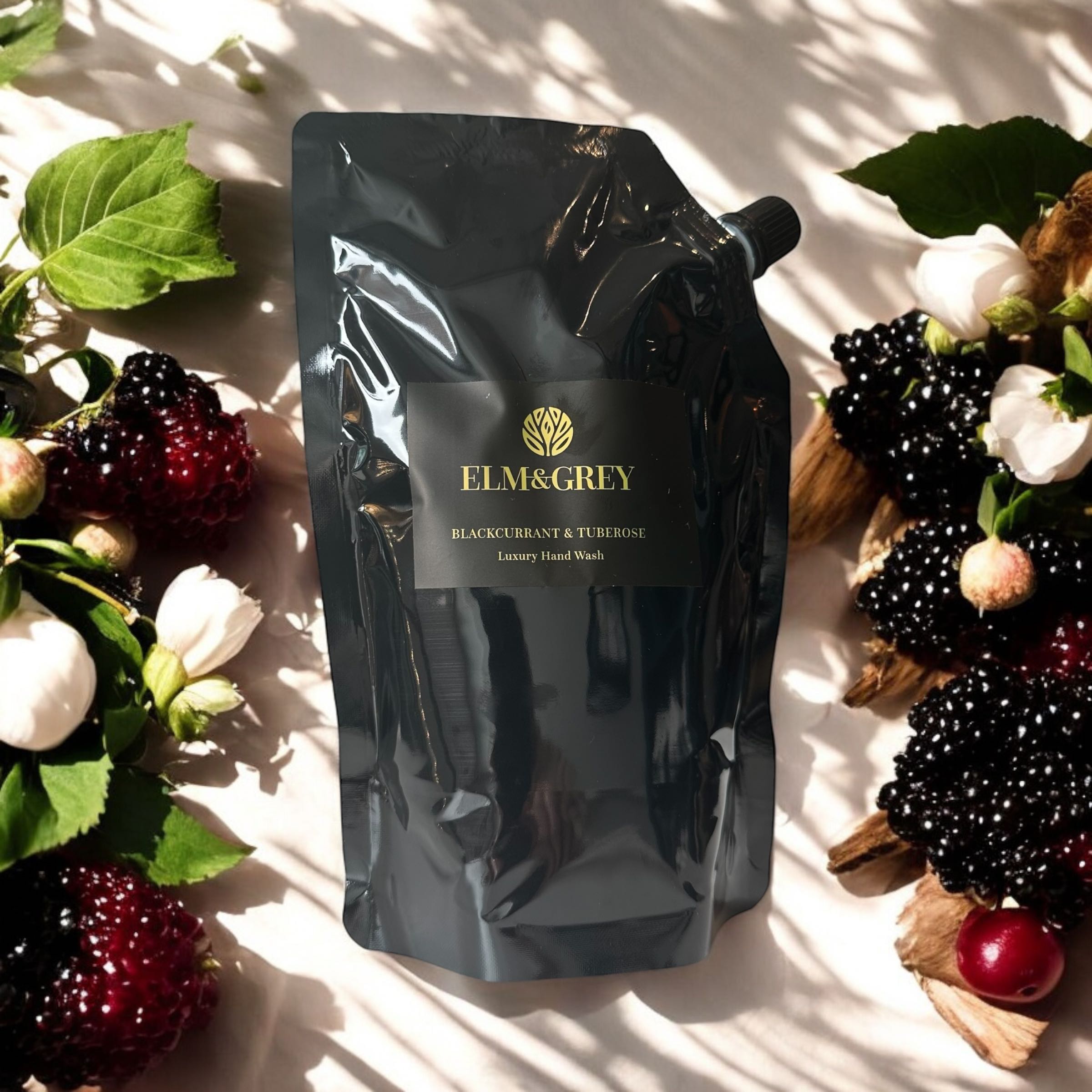 Elm & Grey Blackcurrant & Tuberose Luxury Hand Wash 450ml Black Refill Pouch sitting on a surface with Blackcurrants and Roses in the background
