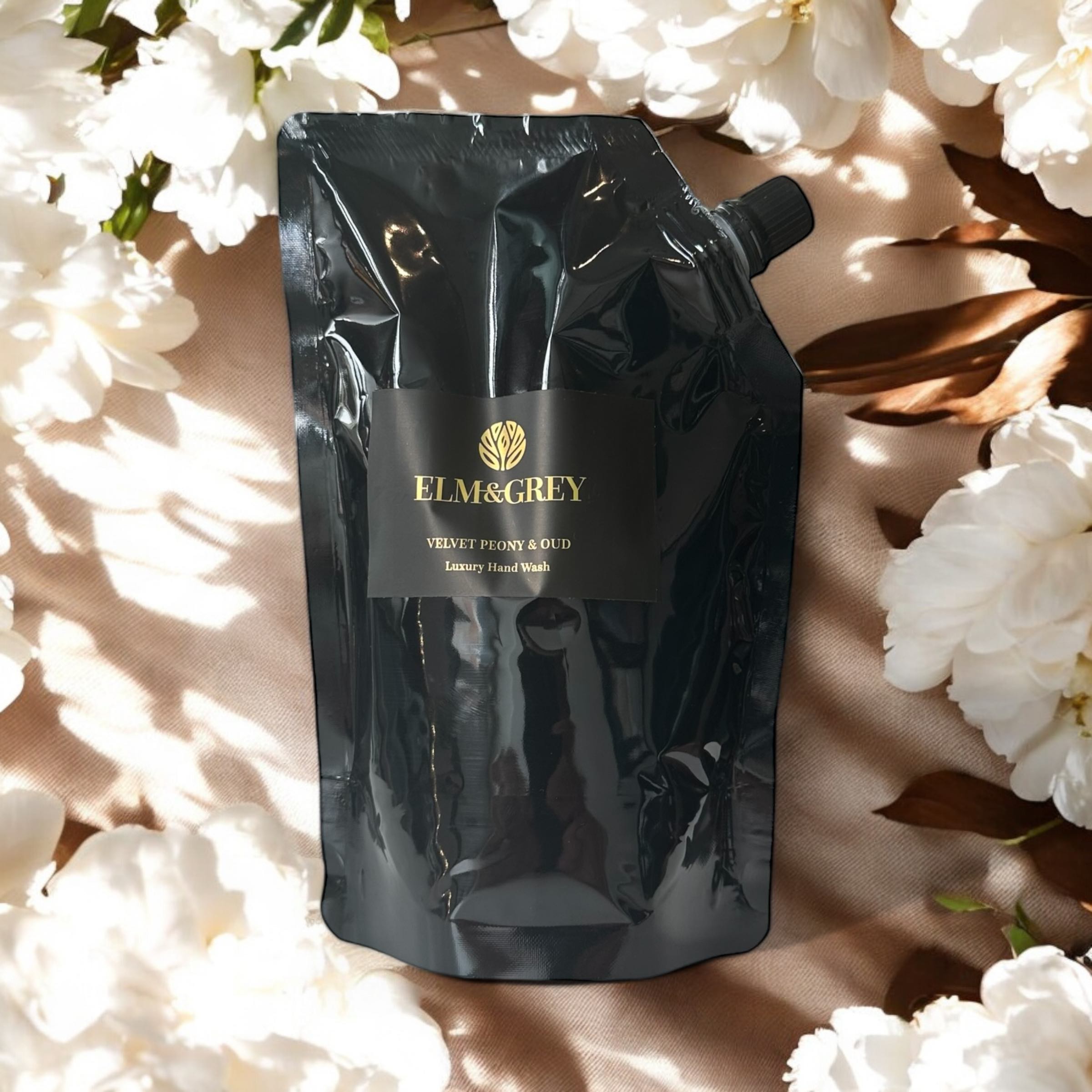 Elm & Grey Velvet Peony & Oud Luxury Hand Wash 450ml Black Refill Pouch sitting on a surface with White Peonies and Oud  in the background