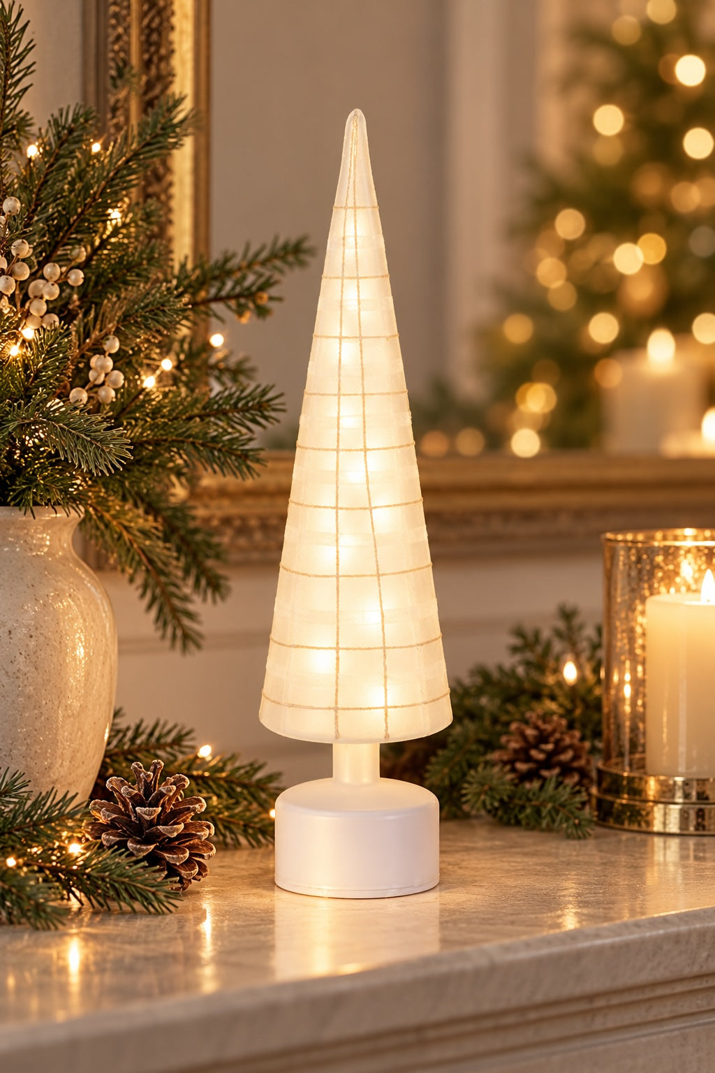 A glowing Frosted rotating Christmas tree glowing isits on a mantelpiece surrounded by holiday greenery, pinecones, and a lit candle in a glass holder.