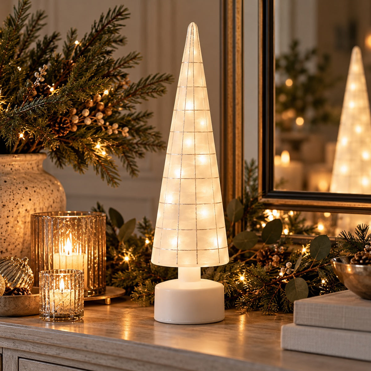 A glowing Frosted rotating Christmas tree glowing isits on a mantelpiece surrounded by holiday greenery, pinecones, and a lit candle in a glass holder.