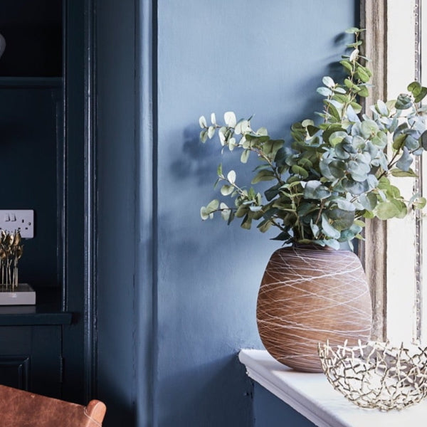 LSA brown boulder vase with greenery on a windowsill against a blue wall