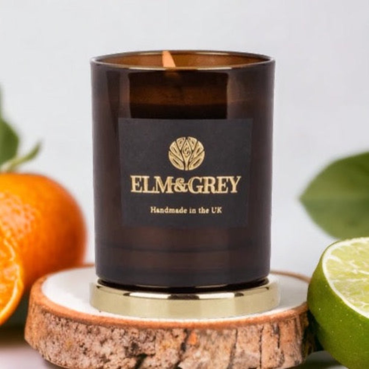Amber lime basil and mandarin candle container on a gold lid surrounded by oranges and limes