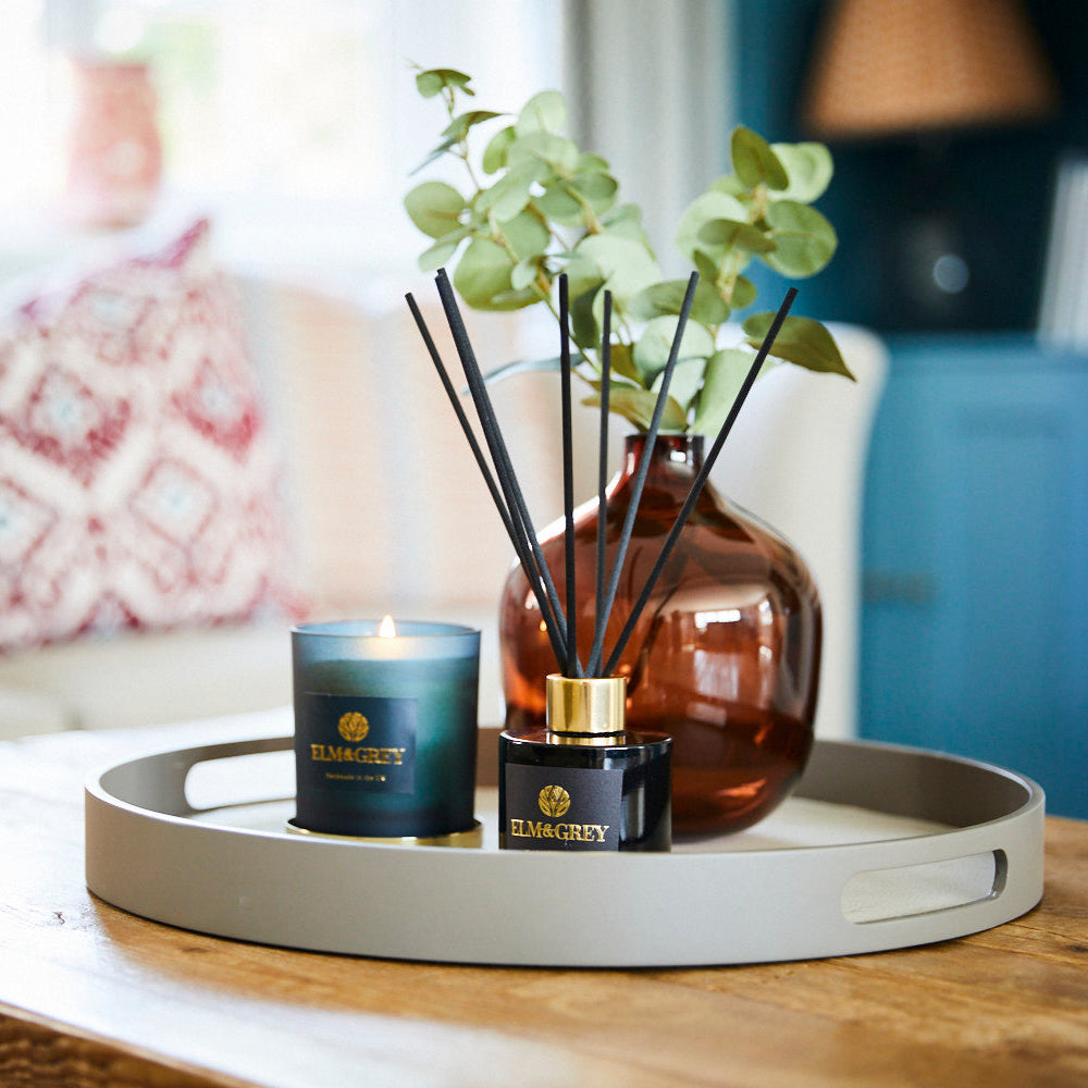 Decorative tray with a candle, diffuser, and flowers on a wooden table.