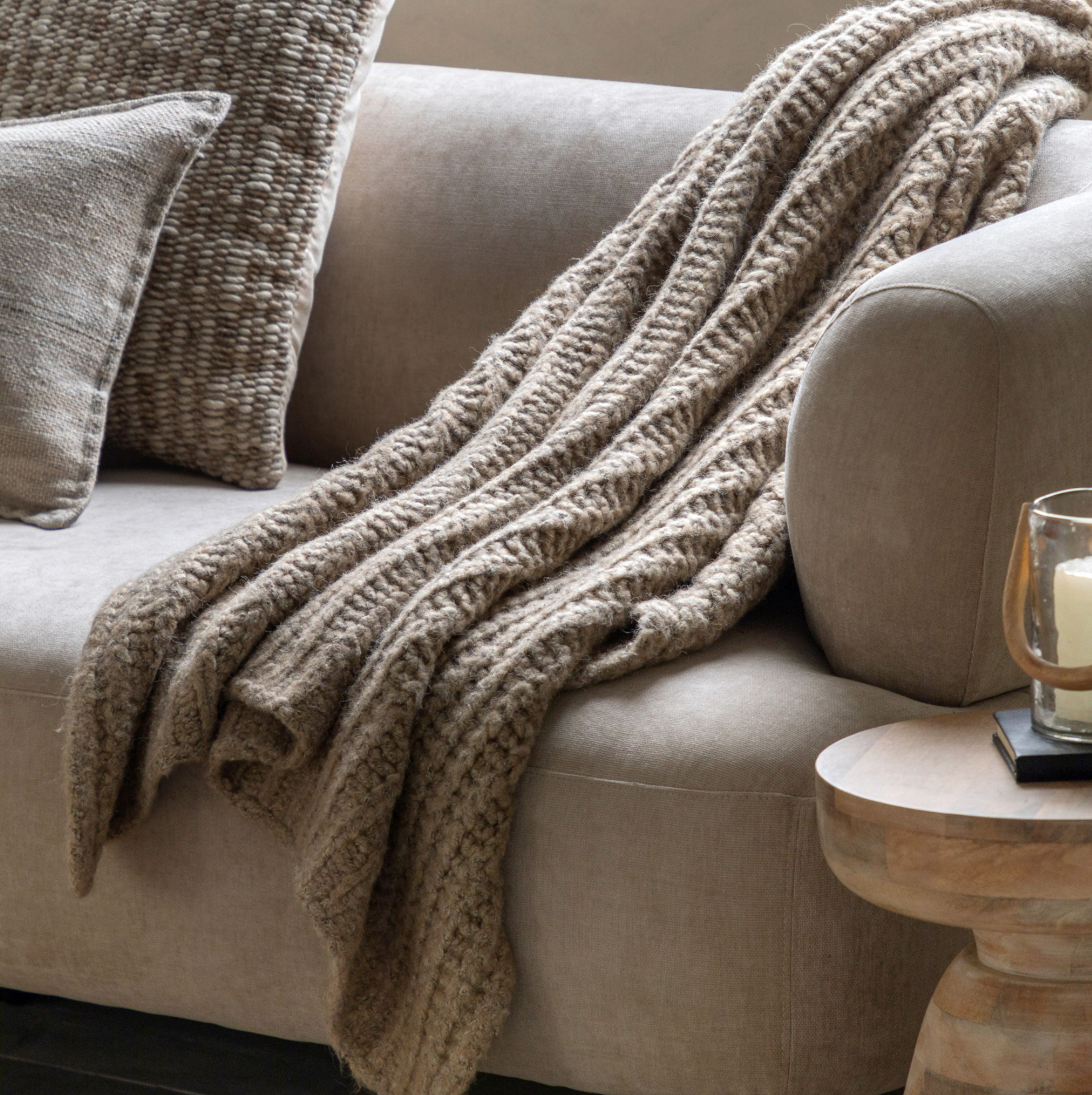 Beige blanket draped over a beige sofa with a side table and candle in the background