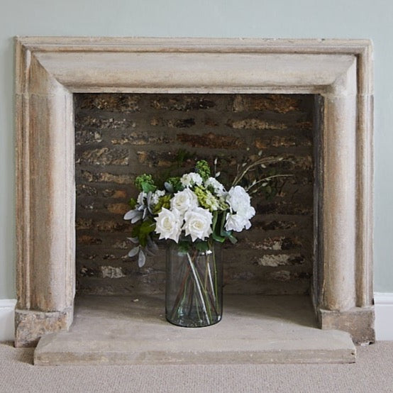 deluxe white roses with pussy willow in a clear glass vase in a stone fireplace