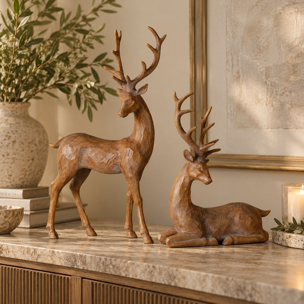 Two decorative deer figurines with a warm brown faux-wood finish, one standing and one reclining, displayed on a marble console table in a styled interior setting.