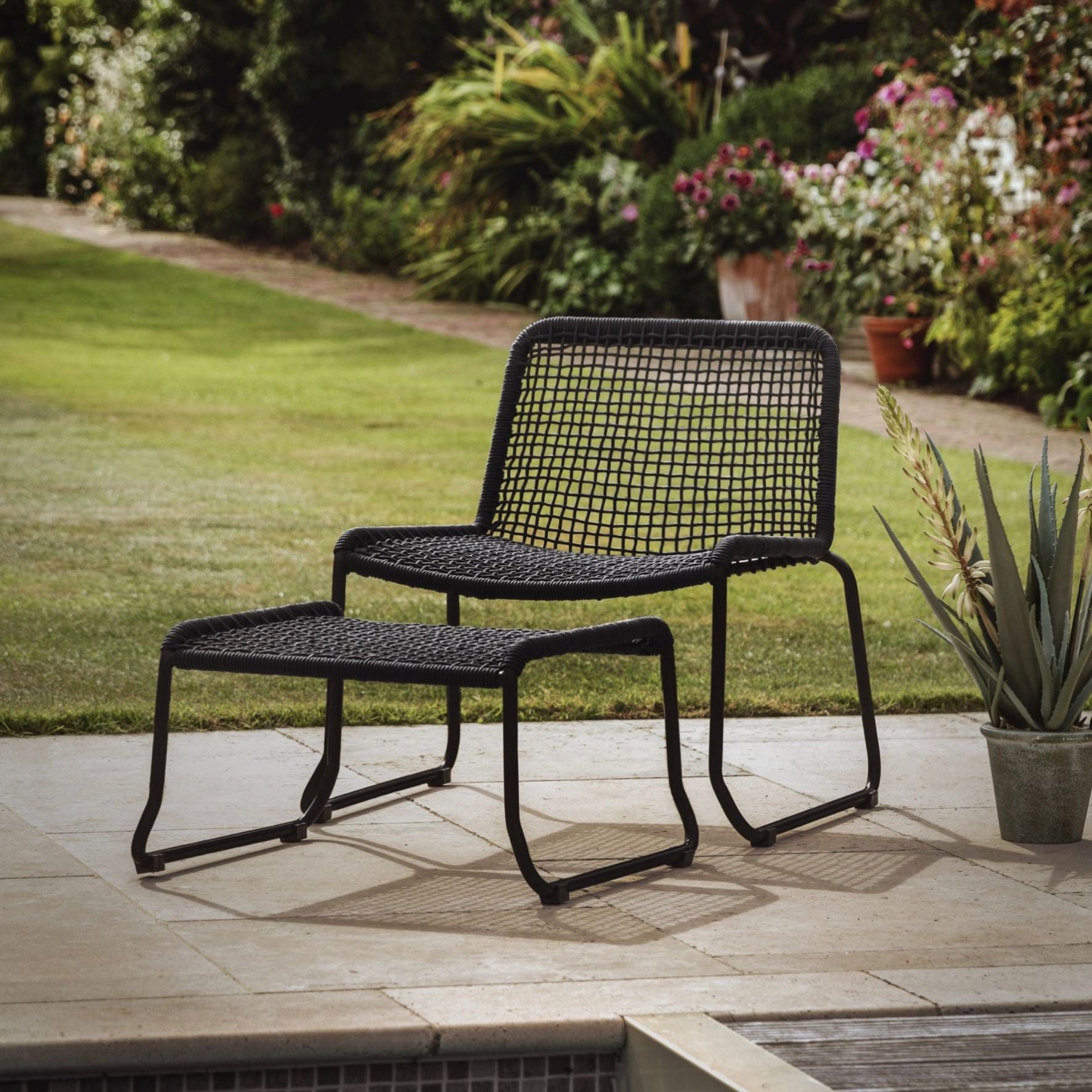Black outdoor chair and ottoman set on a patio with garden background