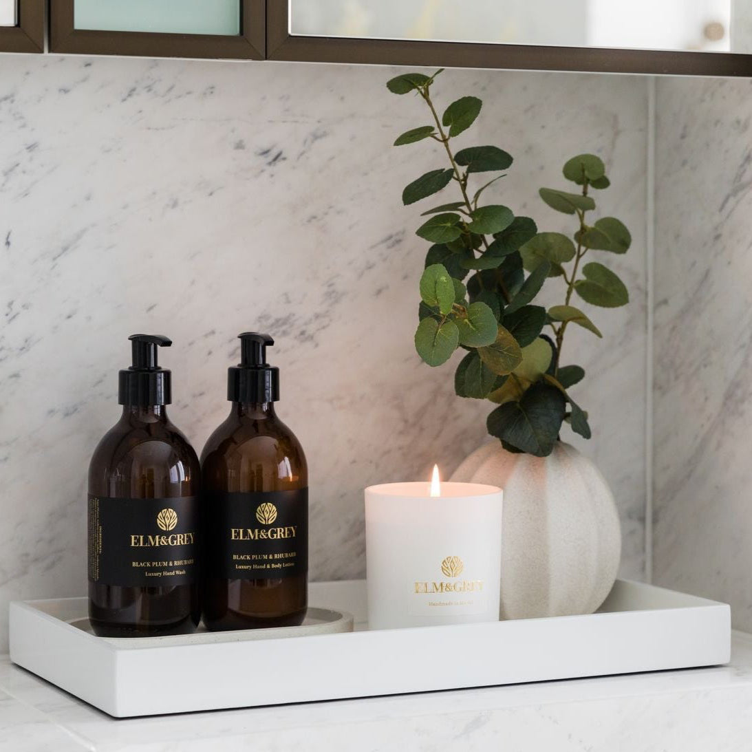 Bathroom counter with two bottles, a candle, and a plant on a white tray.