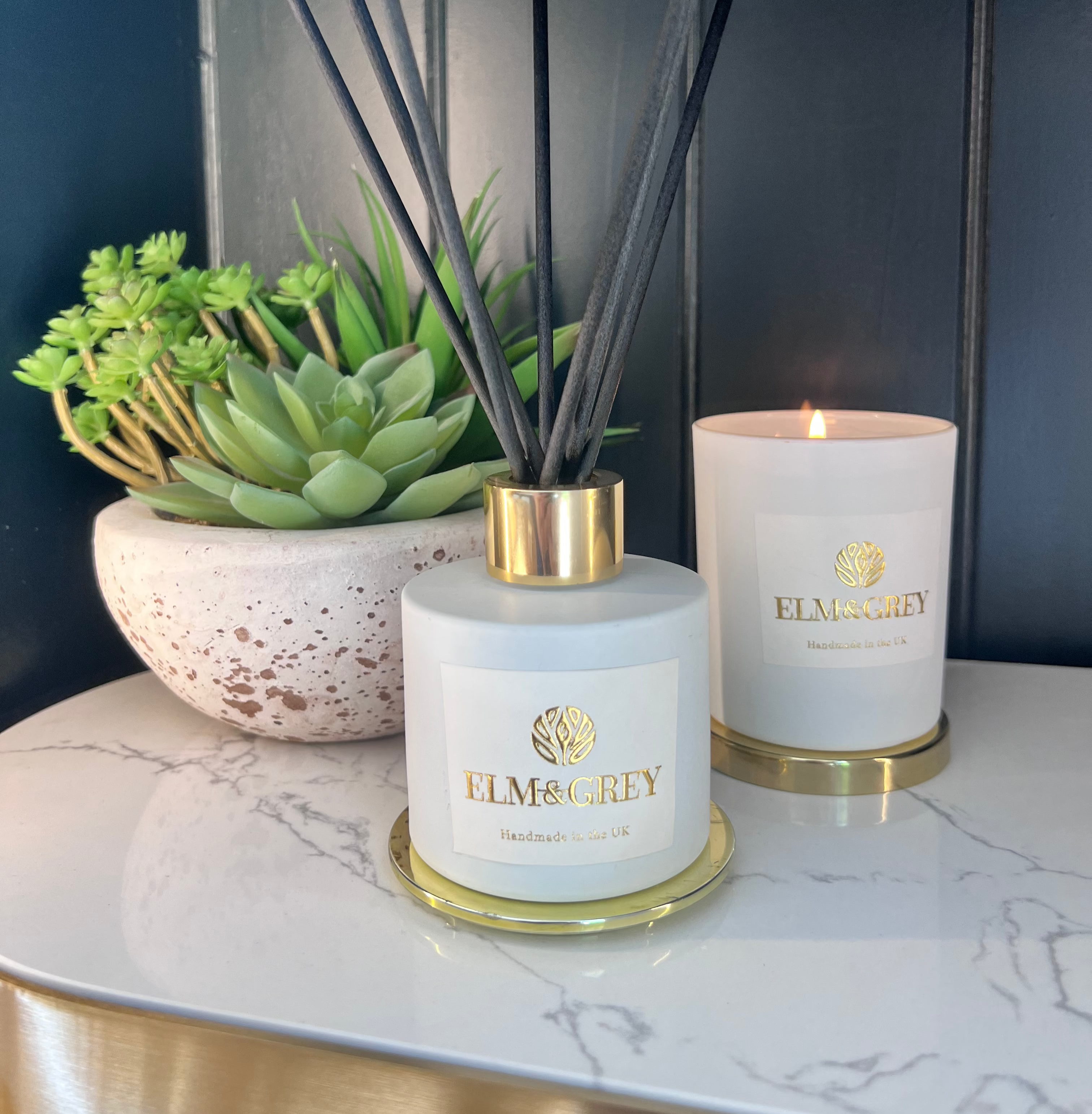 Two diffusers and a candle on a marble surface with a dark background