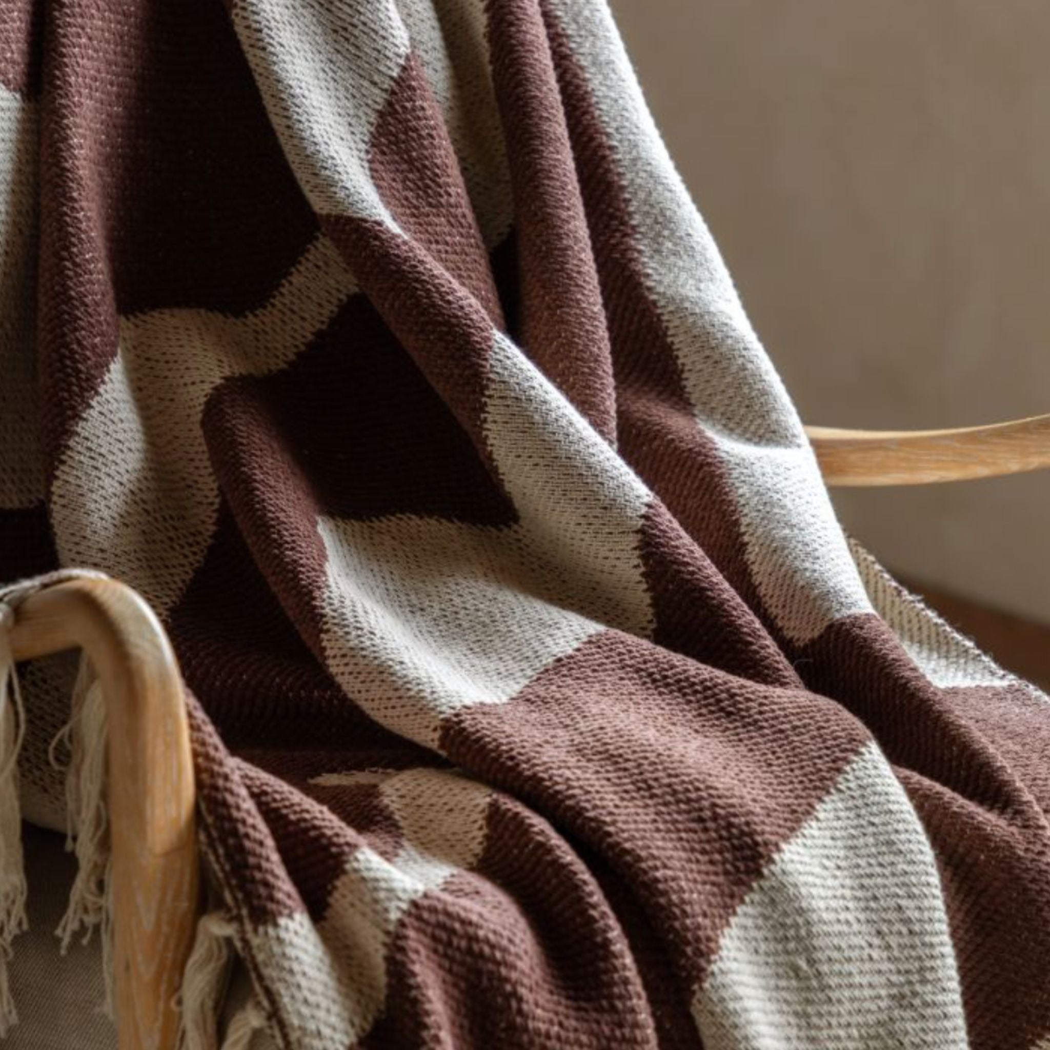 Brown and cream patterned blanket draped over a wooden chair against a neutral background
