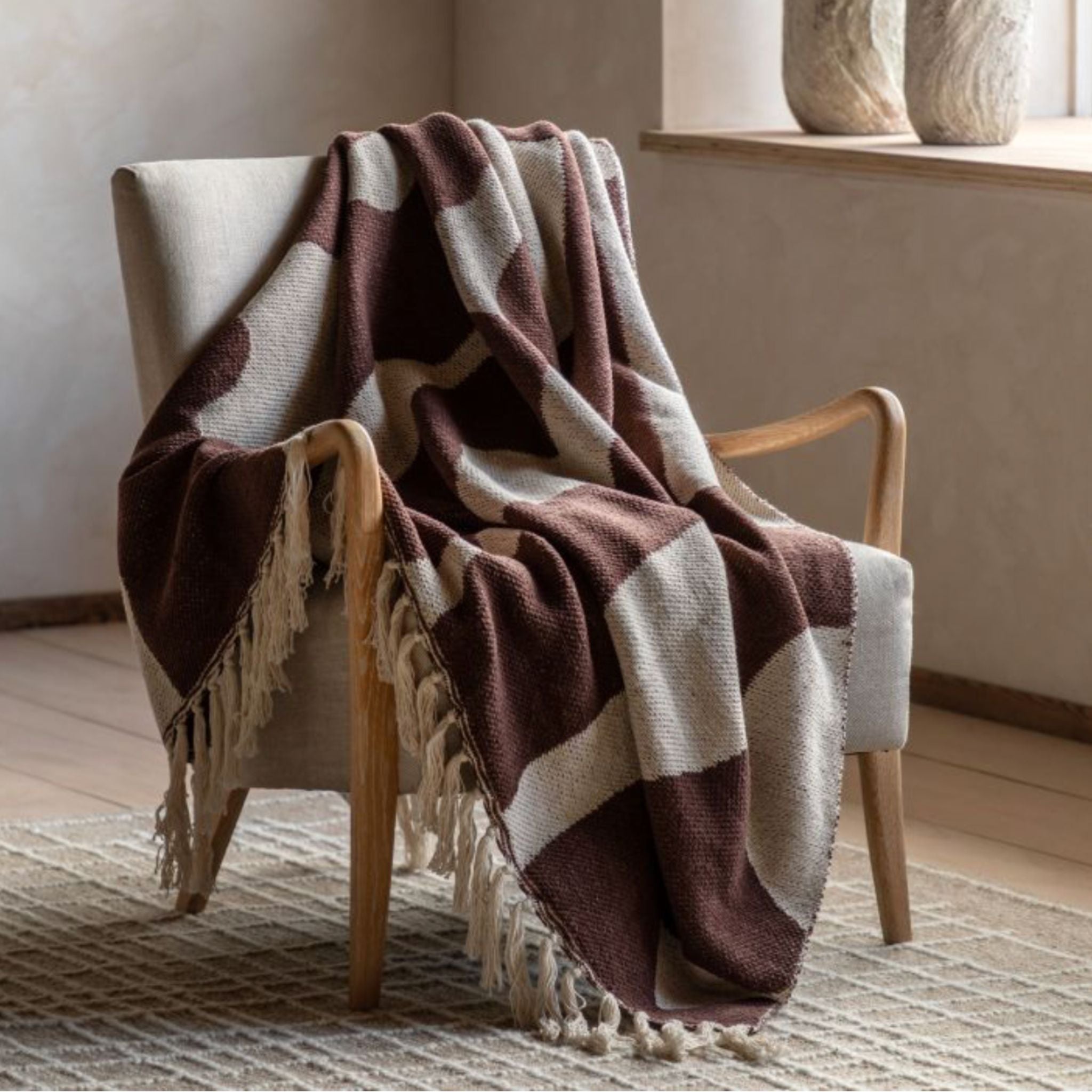 Brown and cream striped blanket draped over a chair in a room with a neutral colour scheme.