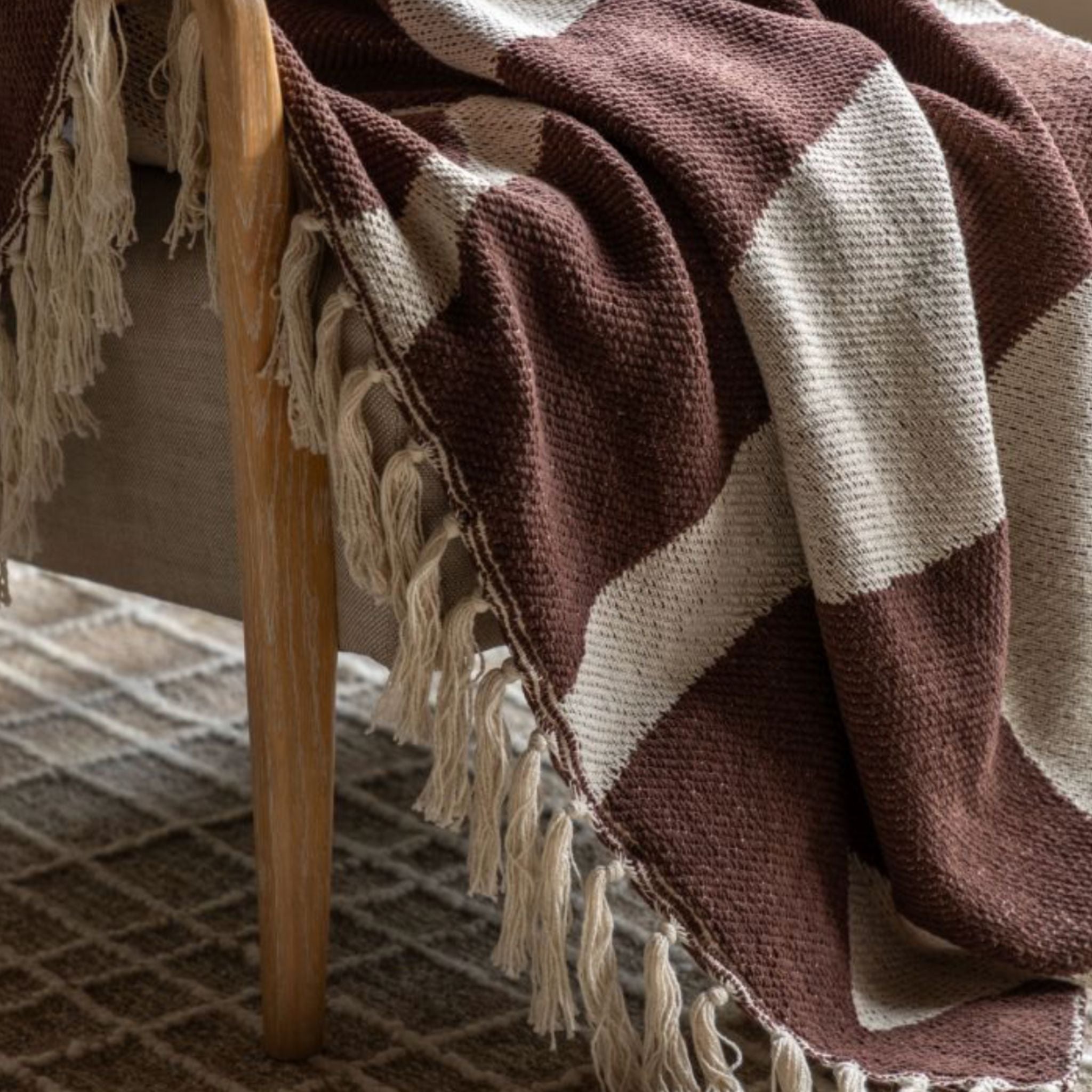 Brown and cream checkered blanket with tassels draped over a wooden chair.
