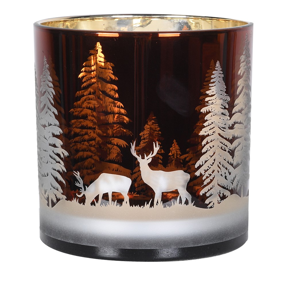 A dark amber glass candle holder featuring a winter forest design with white silhouettes of pine trees, a deer, and a reindeer, with a gold interior rim.