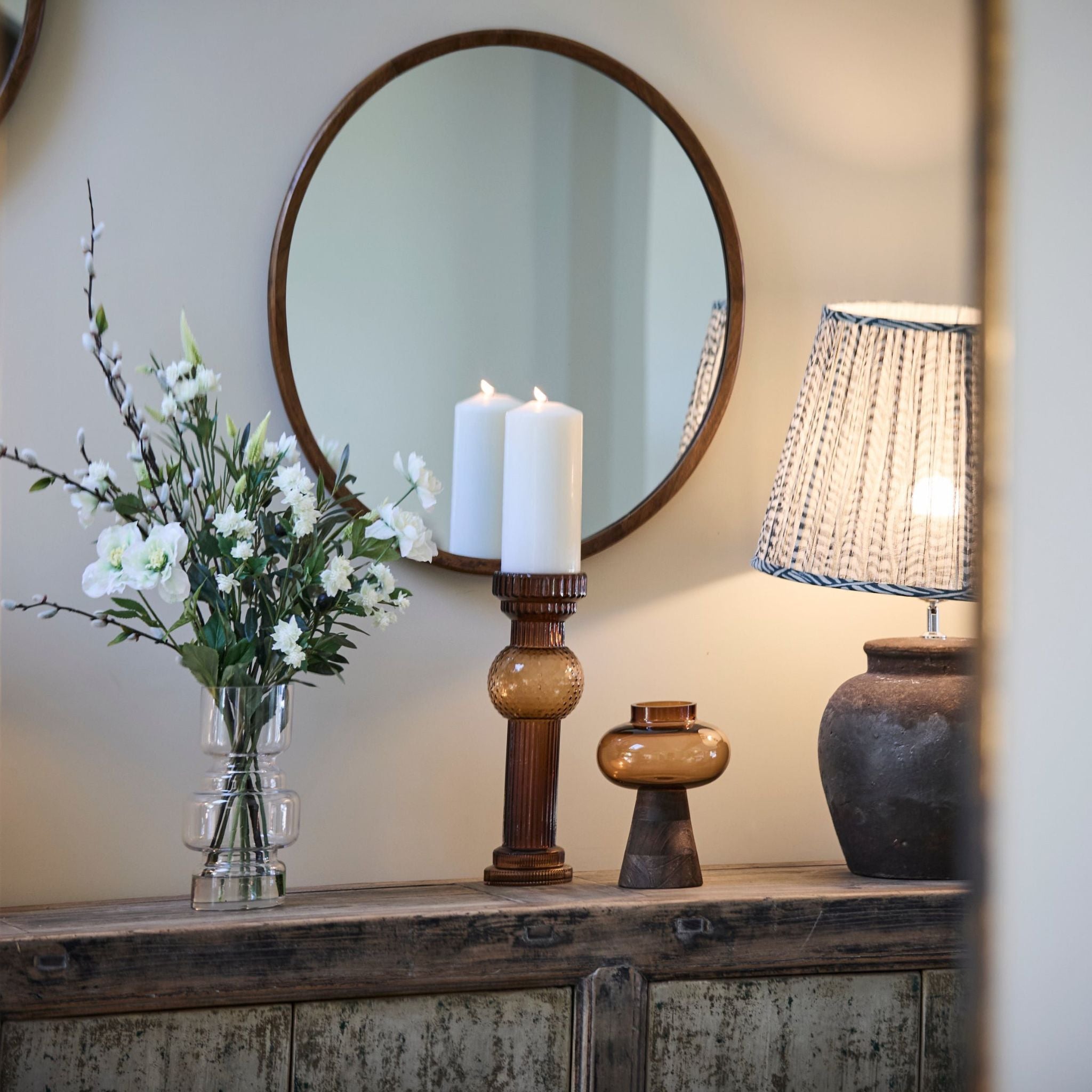 Decorative items including a vase with flowers, candles, and a lamp on a wooden surface.