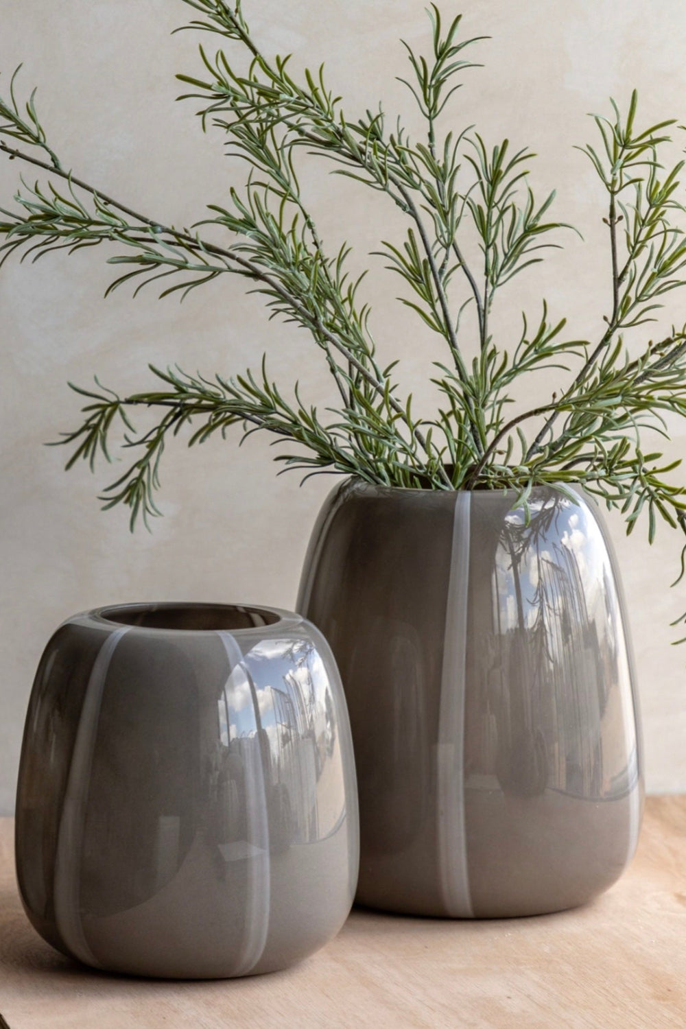 Two taupe stripe vases with greenery on a wooden surface.