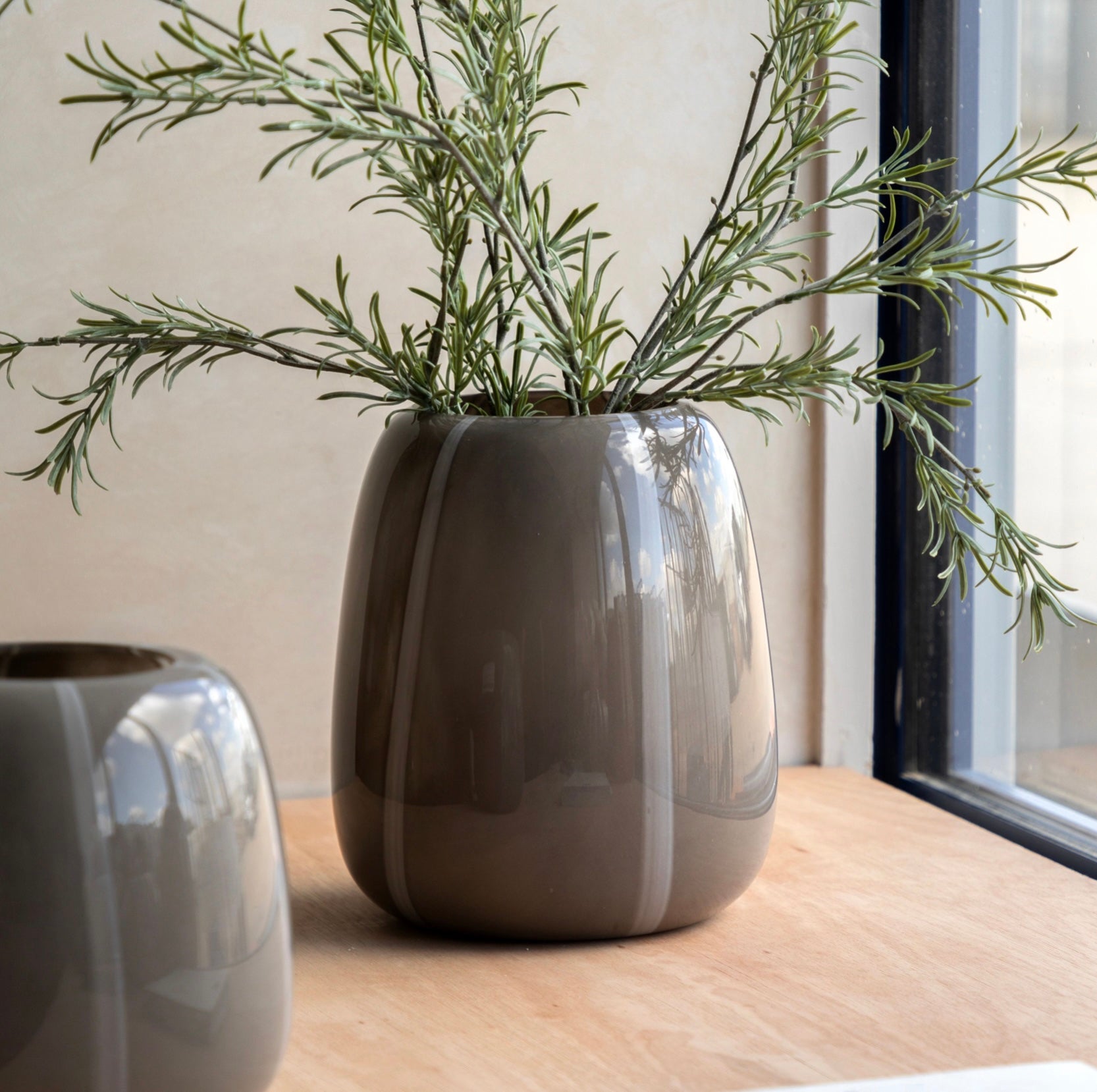 Glossy taupe stripe glass vase with green plant on a wooden surface