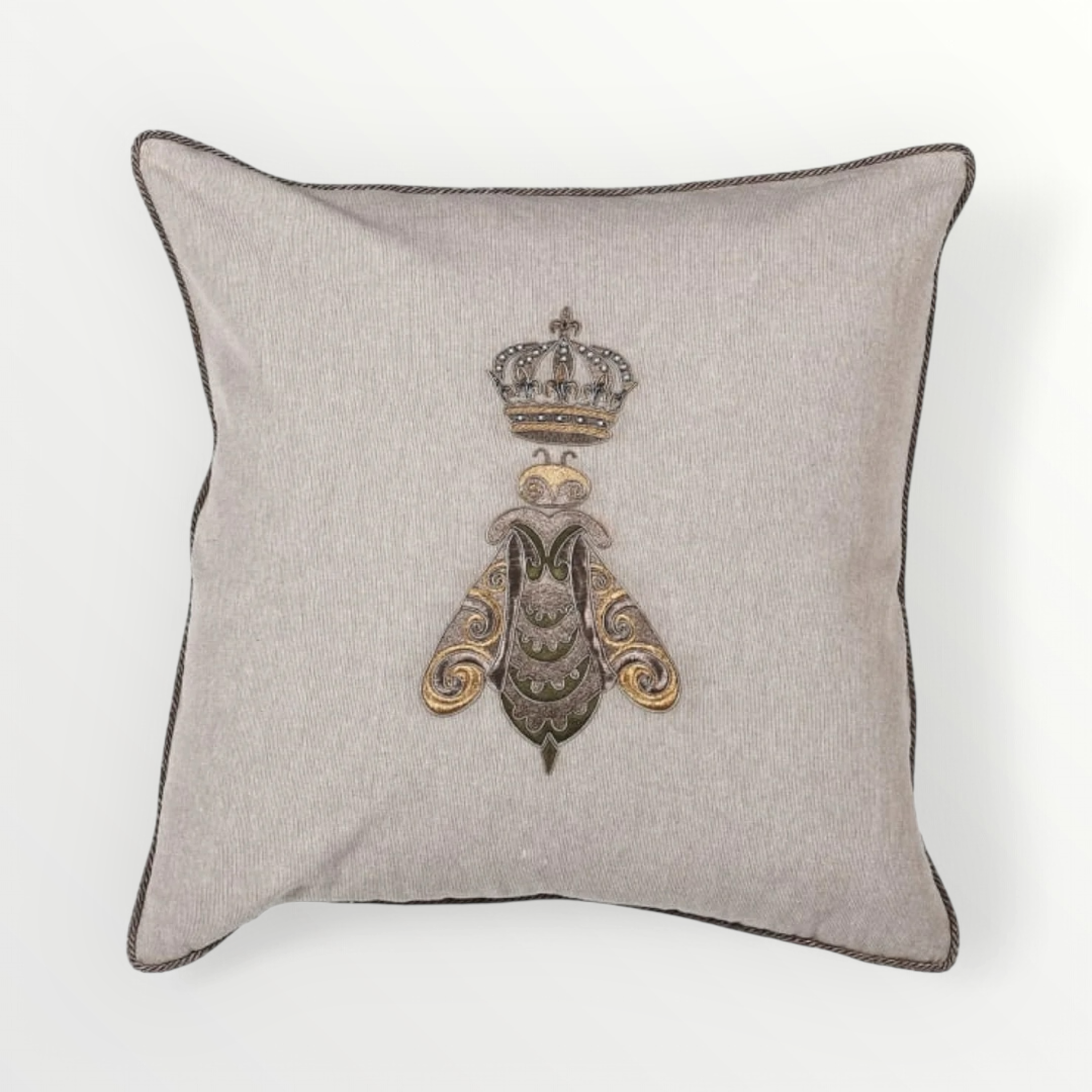 A beige cushion cover featuring a detailed embroidered bee design topped with a crown, highlighted with gold and silver threadwork.