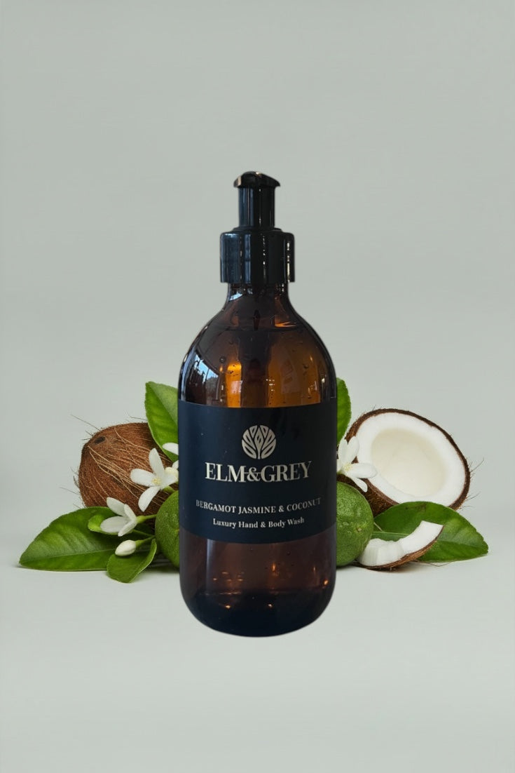 Amber bottle with black cap labeled 'Elm&Grey' on a light grey background with coconuts and leaves.