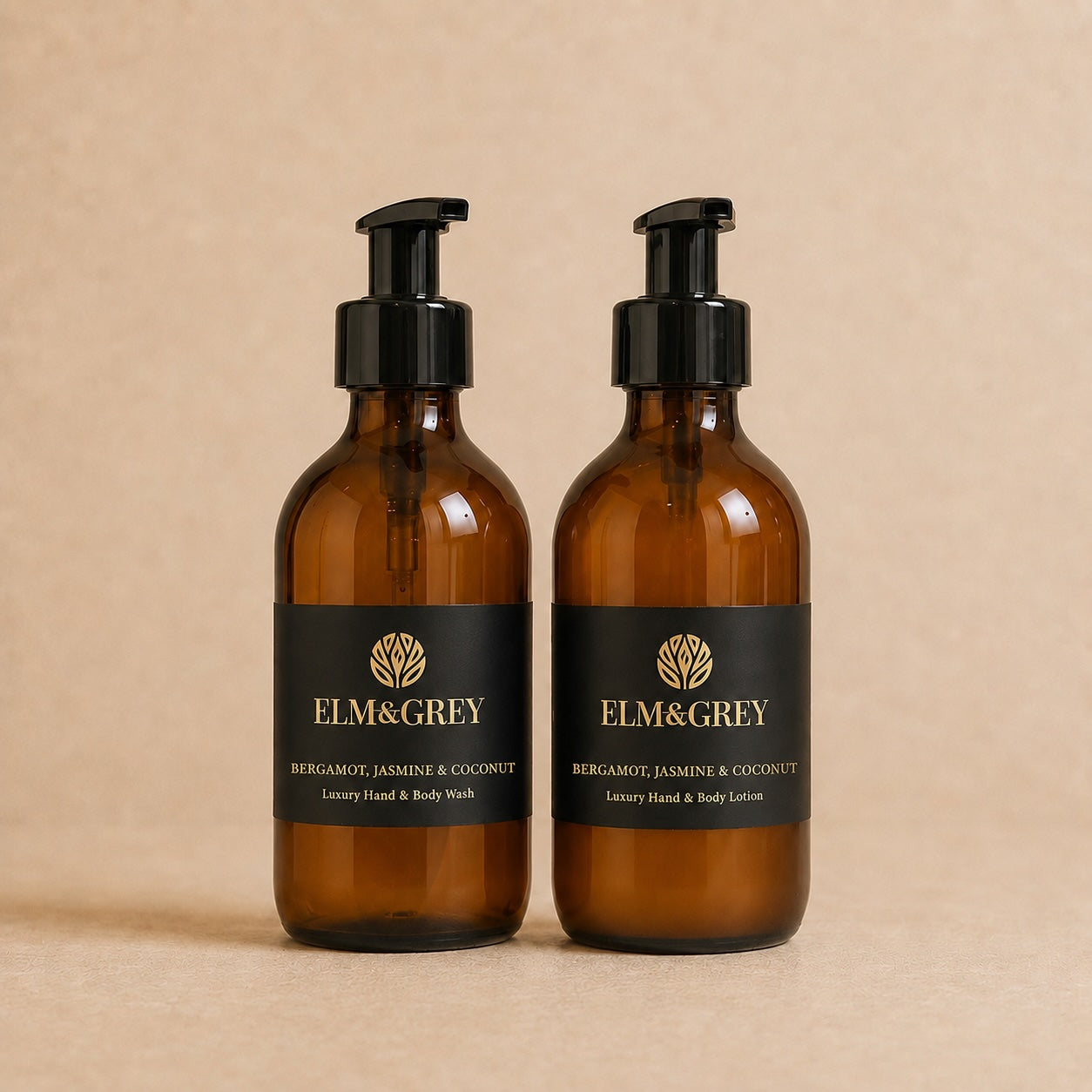 Two amber glass pump bottles with black labels and black pump dispensers, standing side by side on a warm beige background. The labels read ELM&GREY and Bergamot, Jasmine & Coconut Luxury Hand & Body Wash and Body Lotion.