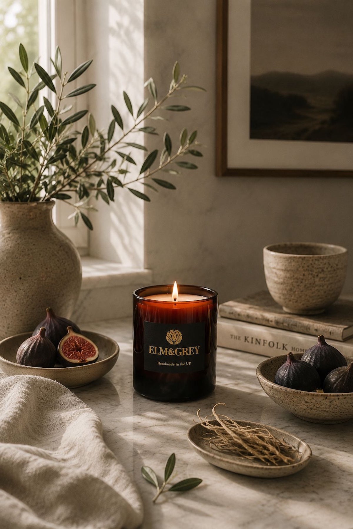 Elm & Grey Black Fig and Vetiver scented candle on marble surface with fresh figs, vetiver root stems and Kinfolk books in natural light