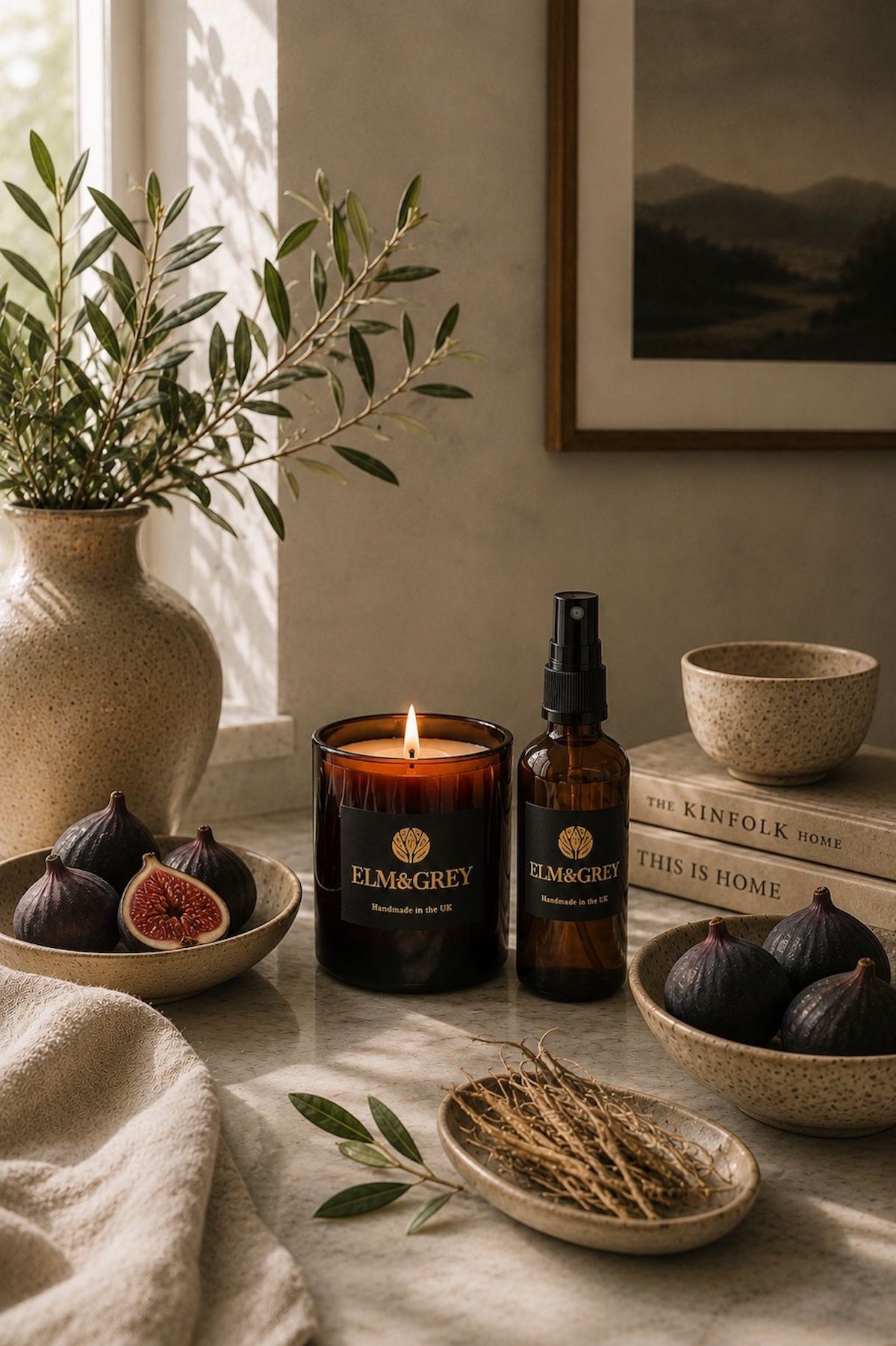 Black Fig & Vetiver luxury scented candle and room spray by Elm & Grey styled with fresh figs, olive branches and natural stone textures in a calm contemporary interior.