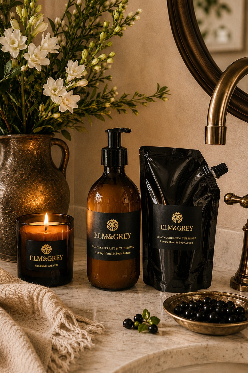 Blackcurrant and tuberose candle, hand lotion bottle and refill pouch styled on a luxurious bathroom countertop with flowers and botanicals.
