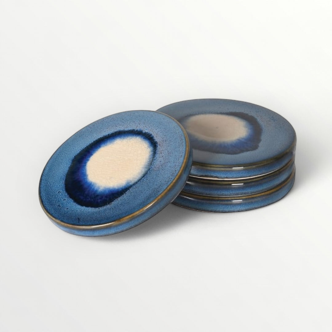 A set of four ceramic coasters with a reactive glaze in blue and ivory tones, displayed against a white background.
