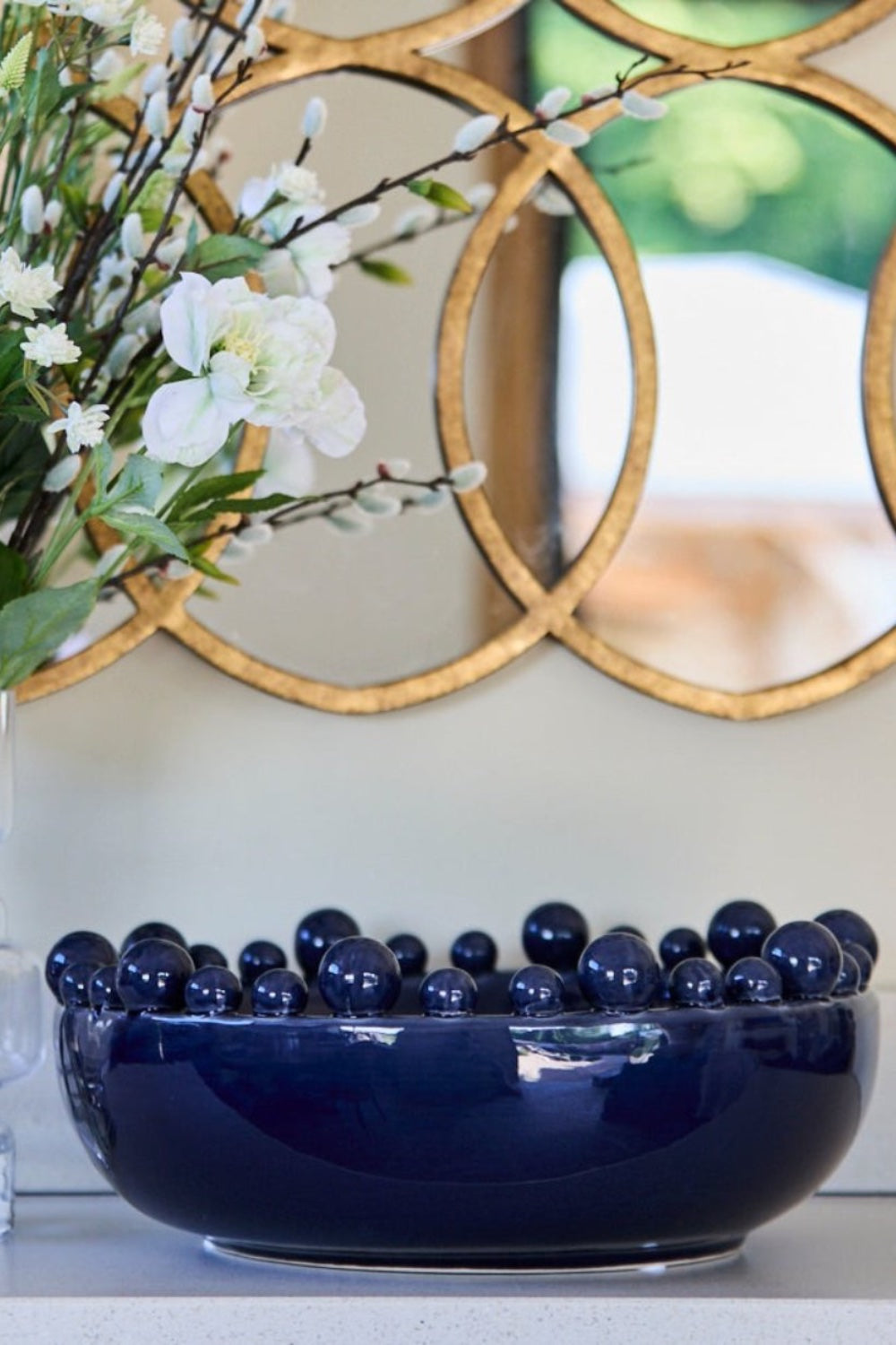 Deep navy bobble-edged ceramic decorative bowl on marble kitchen counter with lit ribbed tealight and olive branches in ribbed ceramic vase — Elm & Grey