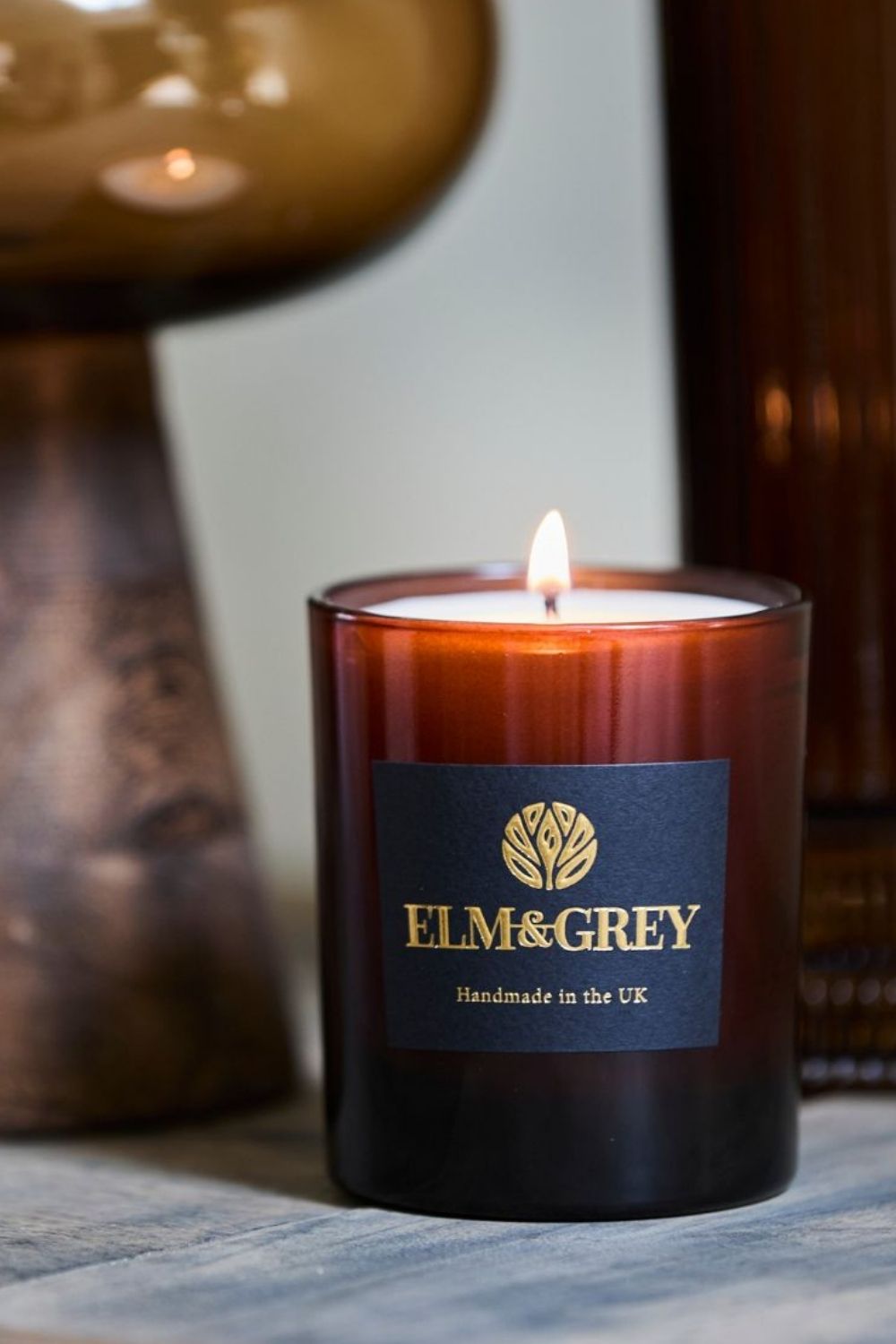 Elm & Grey candle with a flame on a textured surface