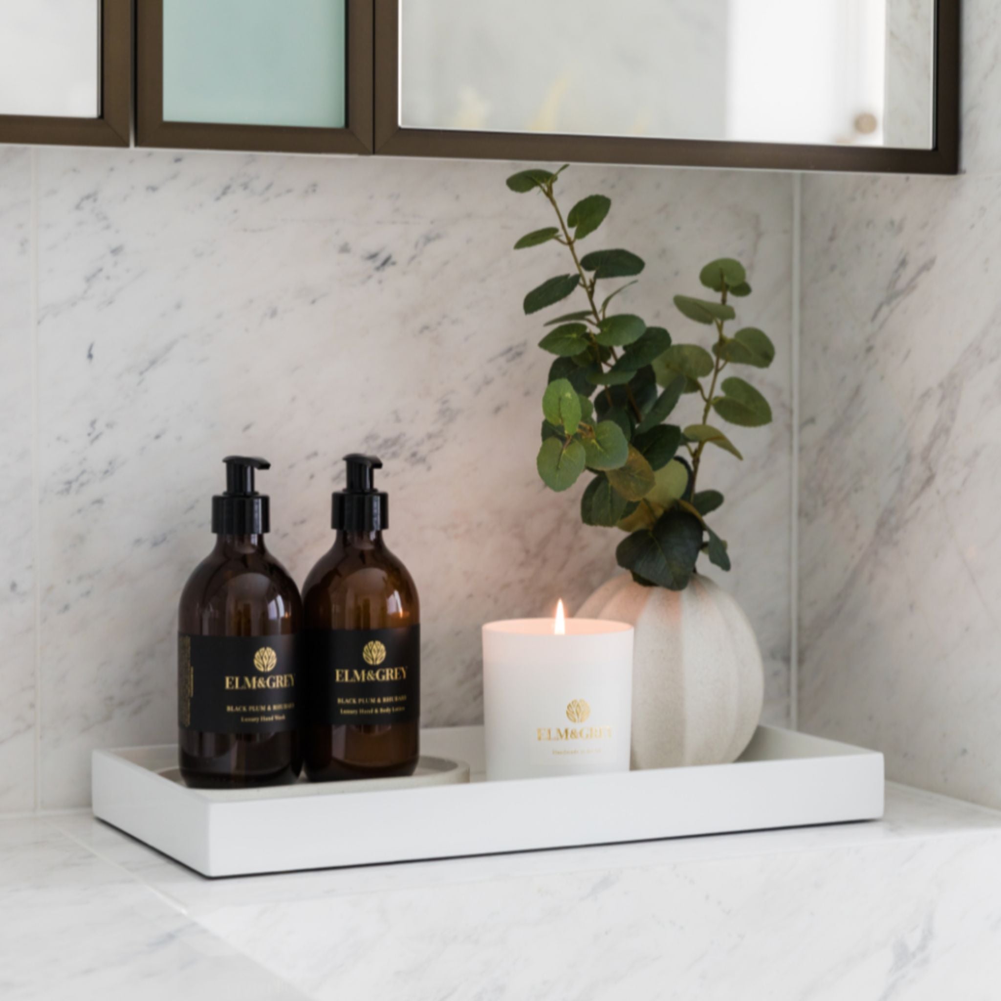 Two bottles and a candle on a white tray with a marble wall background