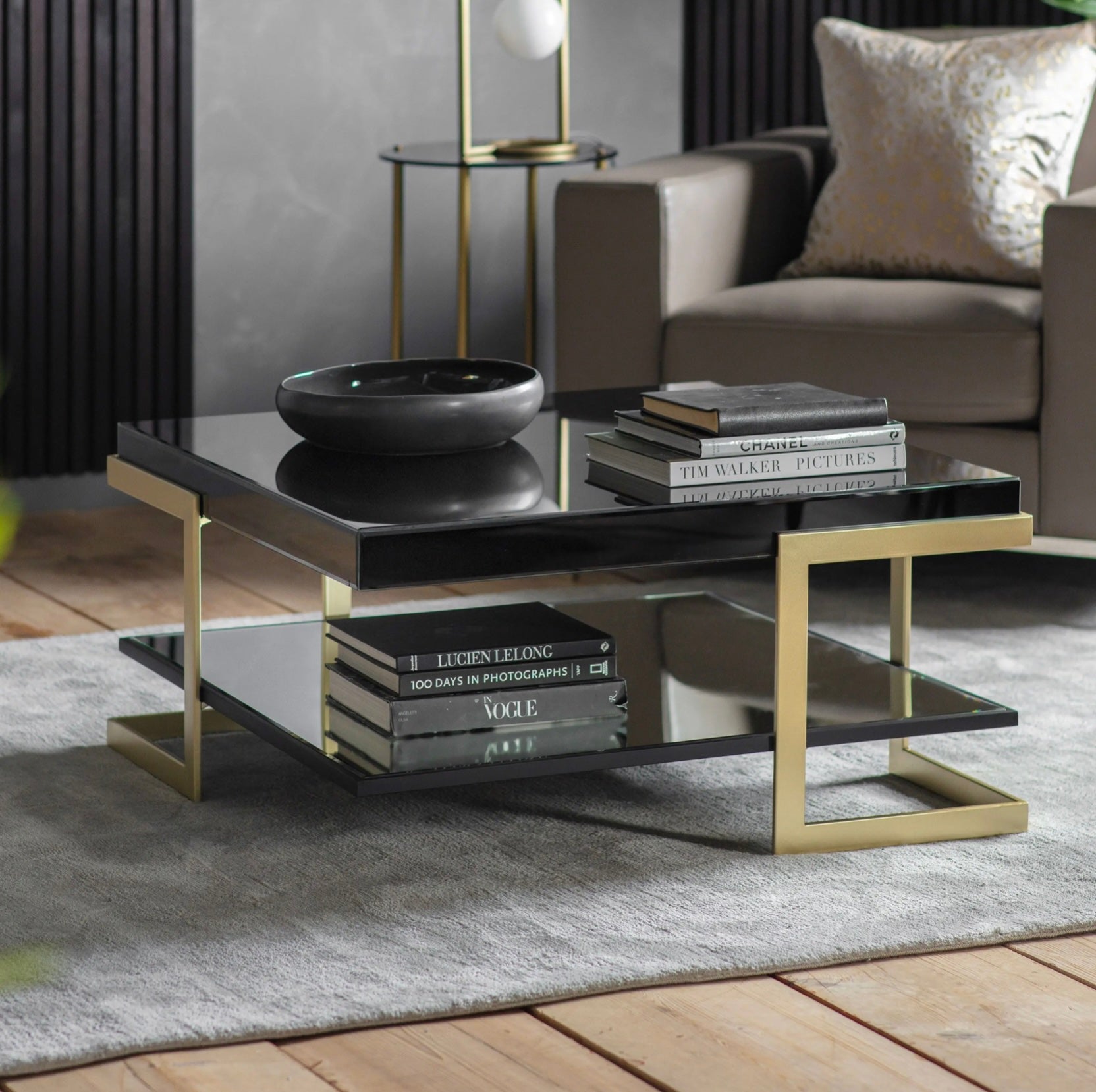 Modern coffee table with gold legs and black glass top in a living room setting.