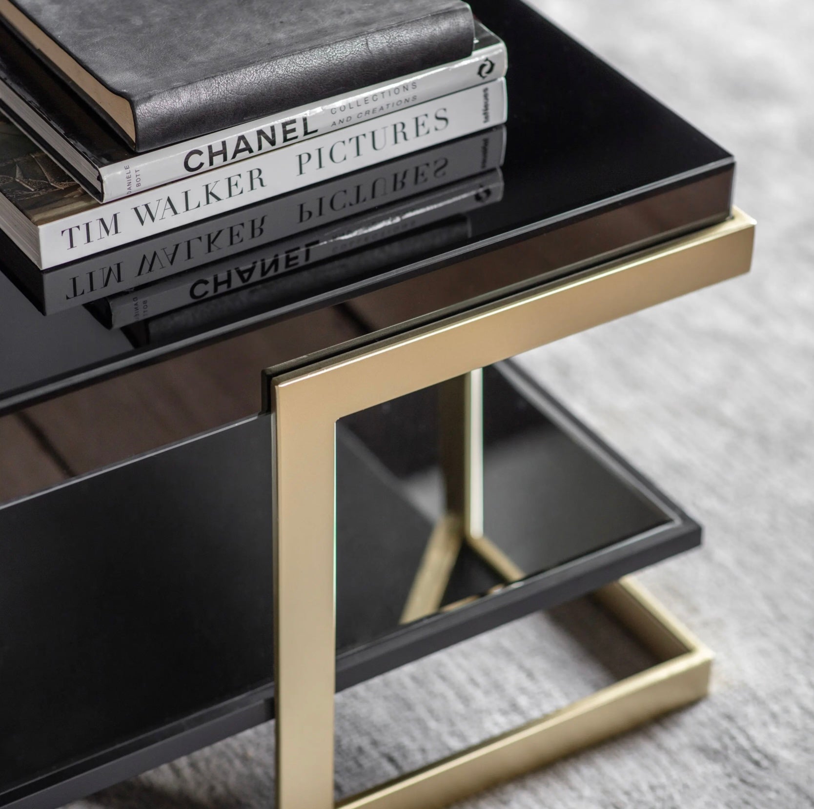 Black glass side table with gold legs holding books on a grey surface