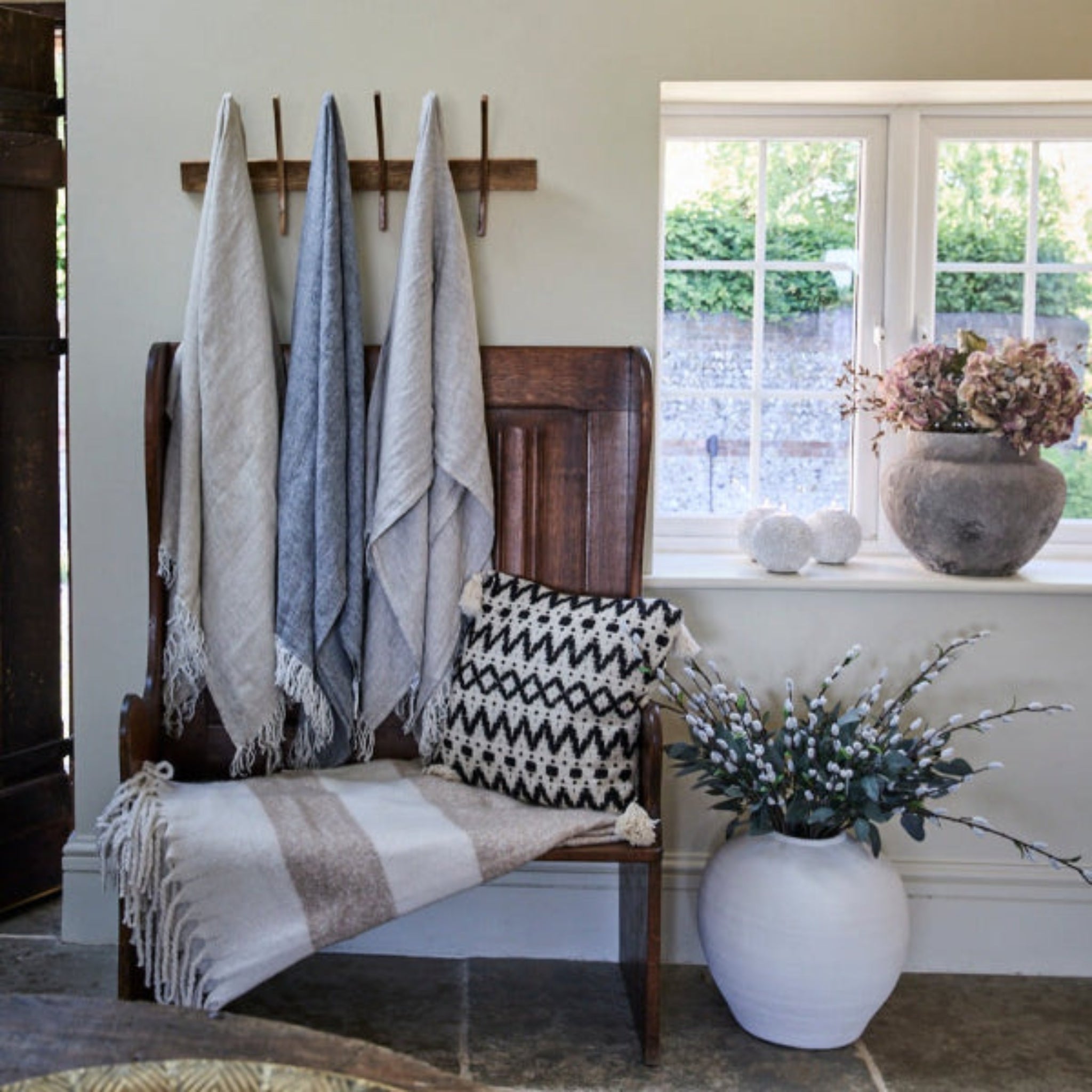 Blankets hanging from hooks a cushion on the seat and a concrete vase on a window sill