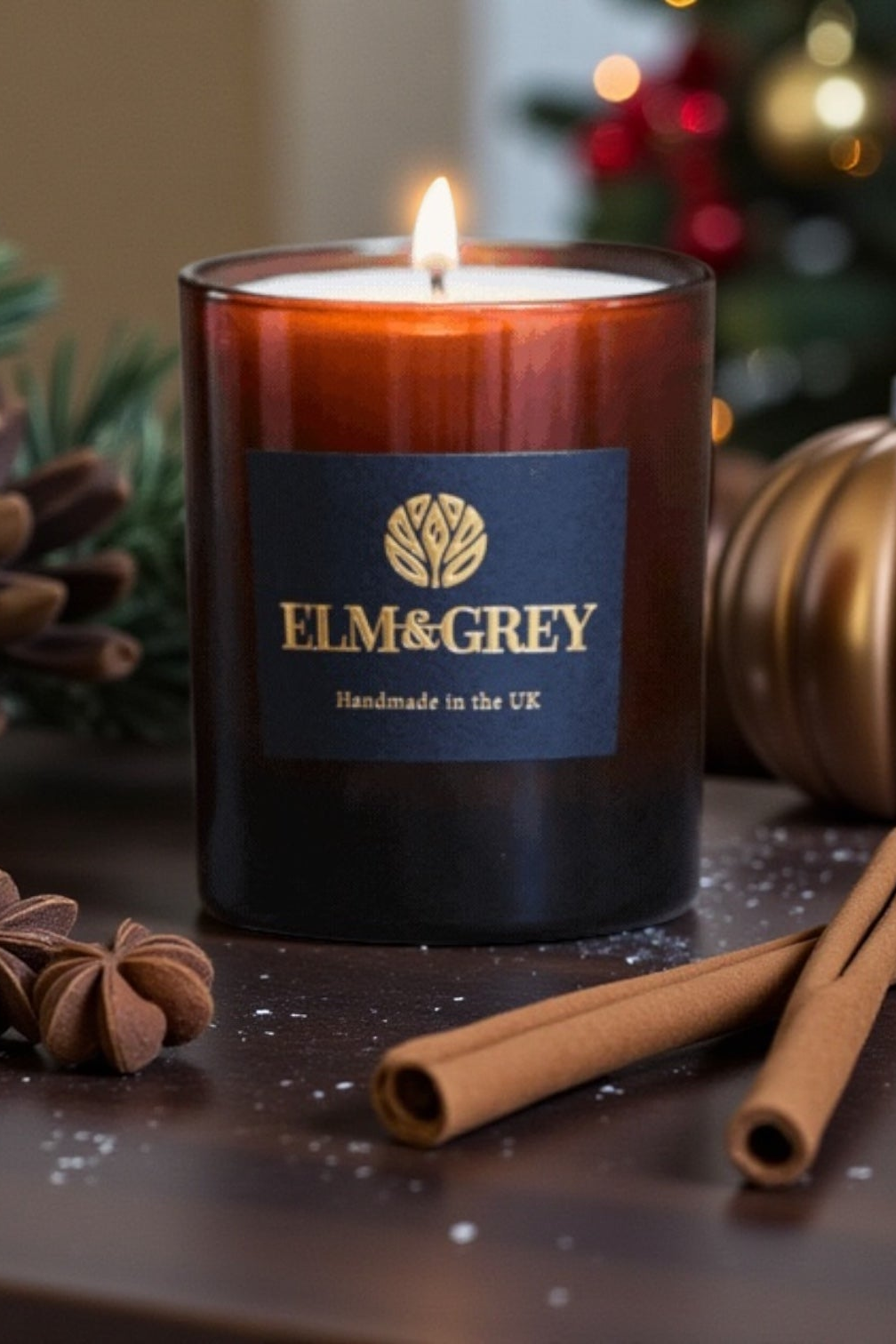 Candle with Elm & Grey label surrounded by cinnamon sticks and pine cones on a wooden surface.