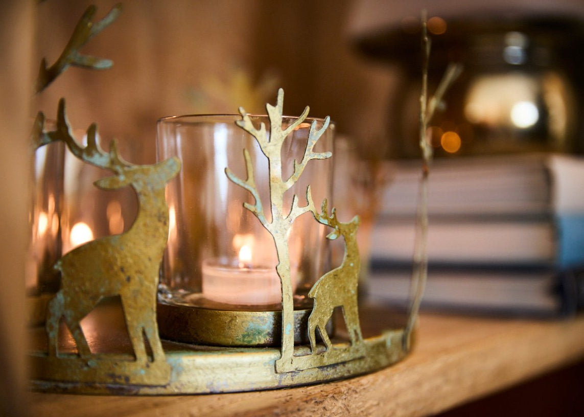 Decorative candle holder with deer designs on a wooden surface.
