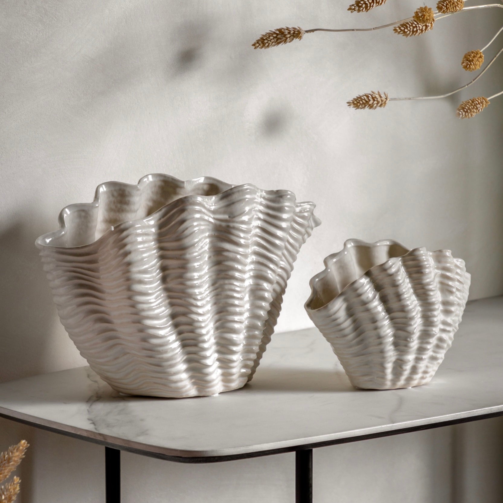 Two white ceramic shell-shaped vases on a marble surface with a neutral background