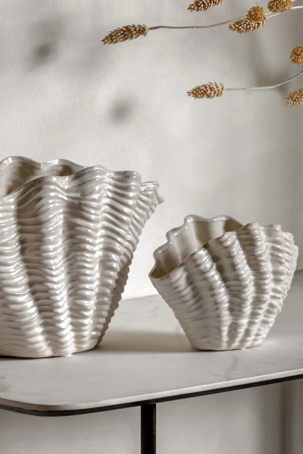 Two shell-shaped ceramic vases on a marble surface with a neutral background