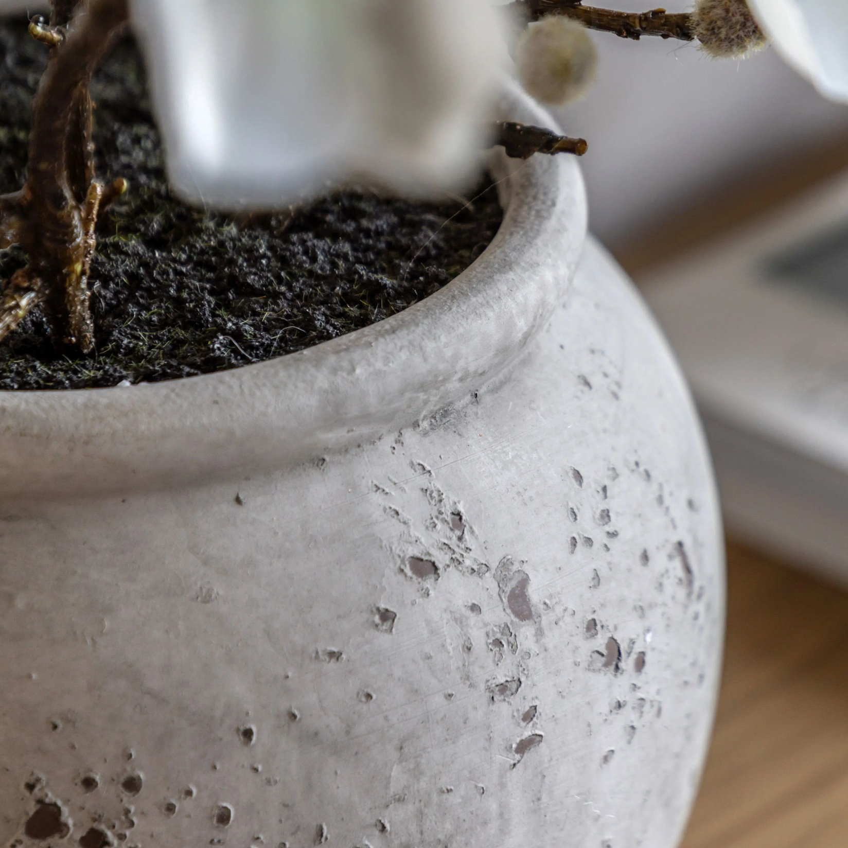 Close-up of a textured gray pot with soil and plant elements on a wooden surface.