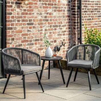 Outdoor patio set with two chairs and a small table against a brick wall.