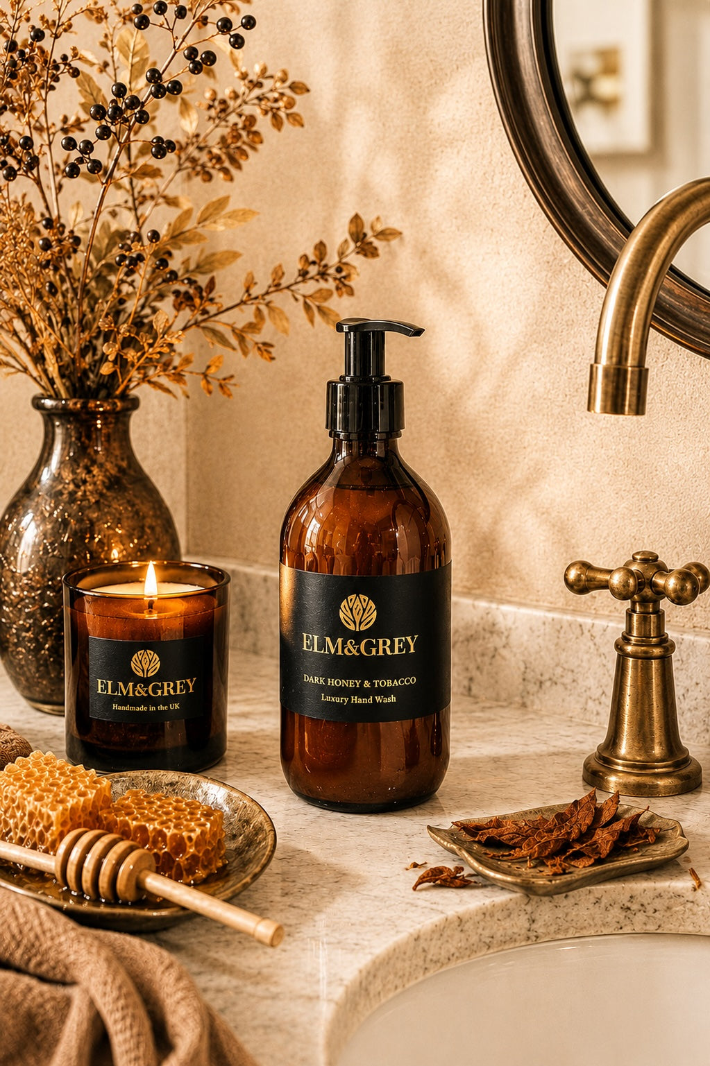Elm & Grey Dark Honey and Tobacco luxury hand wash on marble bathroom surface with lit candle, honeycomb with honey dipper and tobacco pieces beside brass tap in candlelight