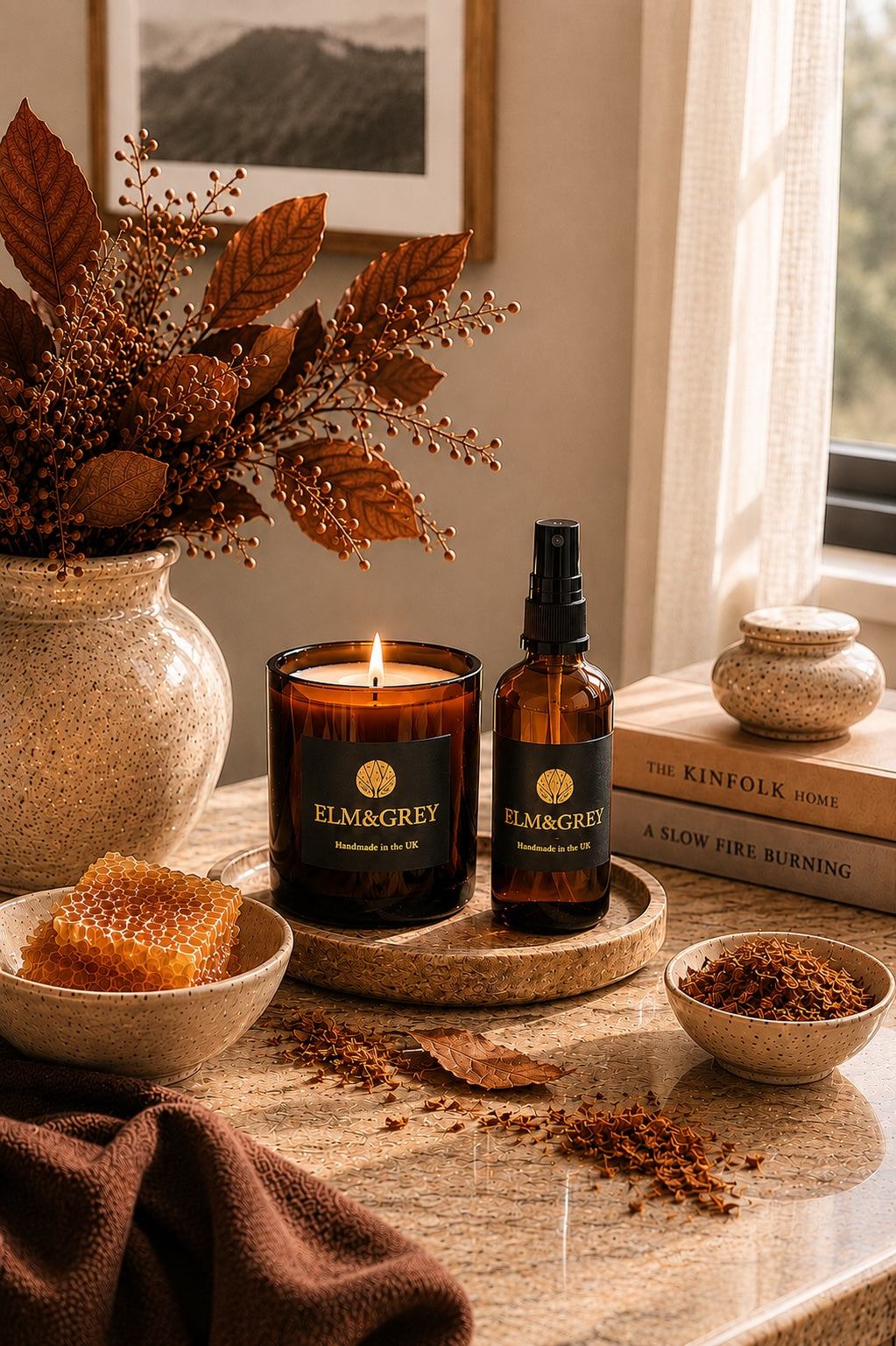 Elm & Grey Dark Honey and Tobacco scented candle and room spray on a round tray styled with honeycomb, tobacco pieces and autumnal copper foliage in warm natural light