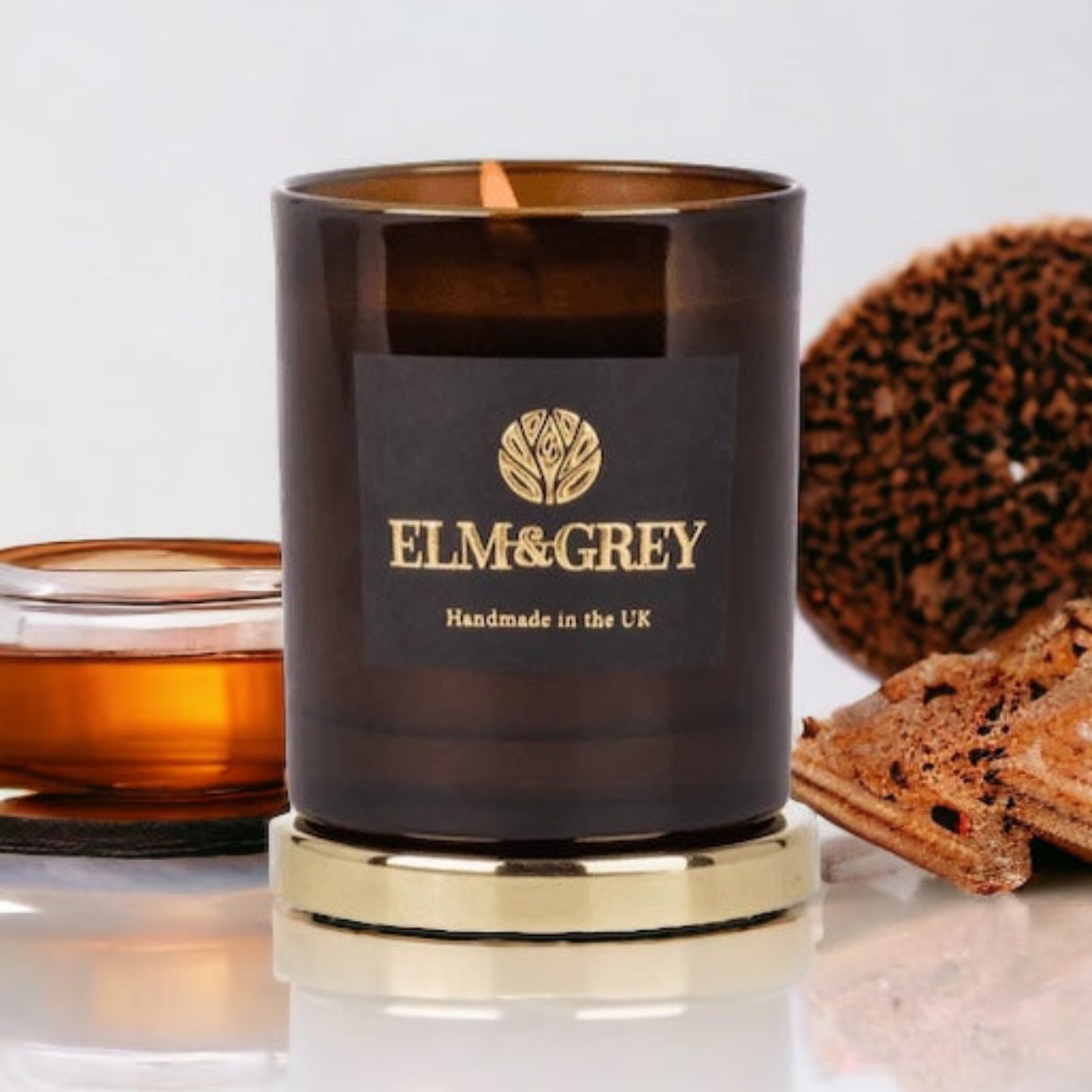 Amber candle standing on a gold lid and surrounded bt honey and tobacco leaf