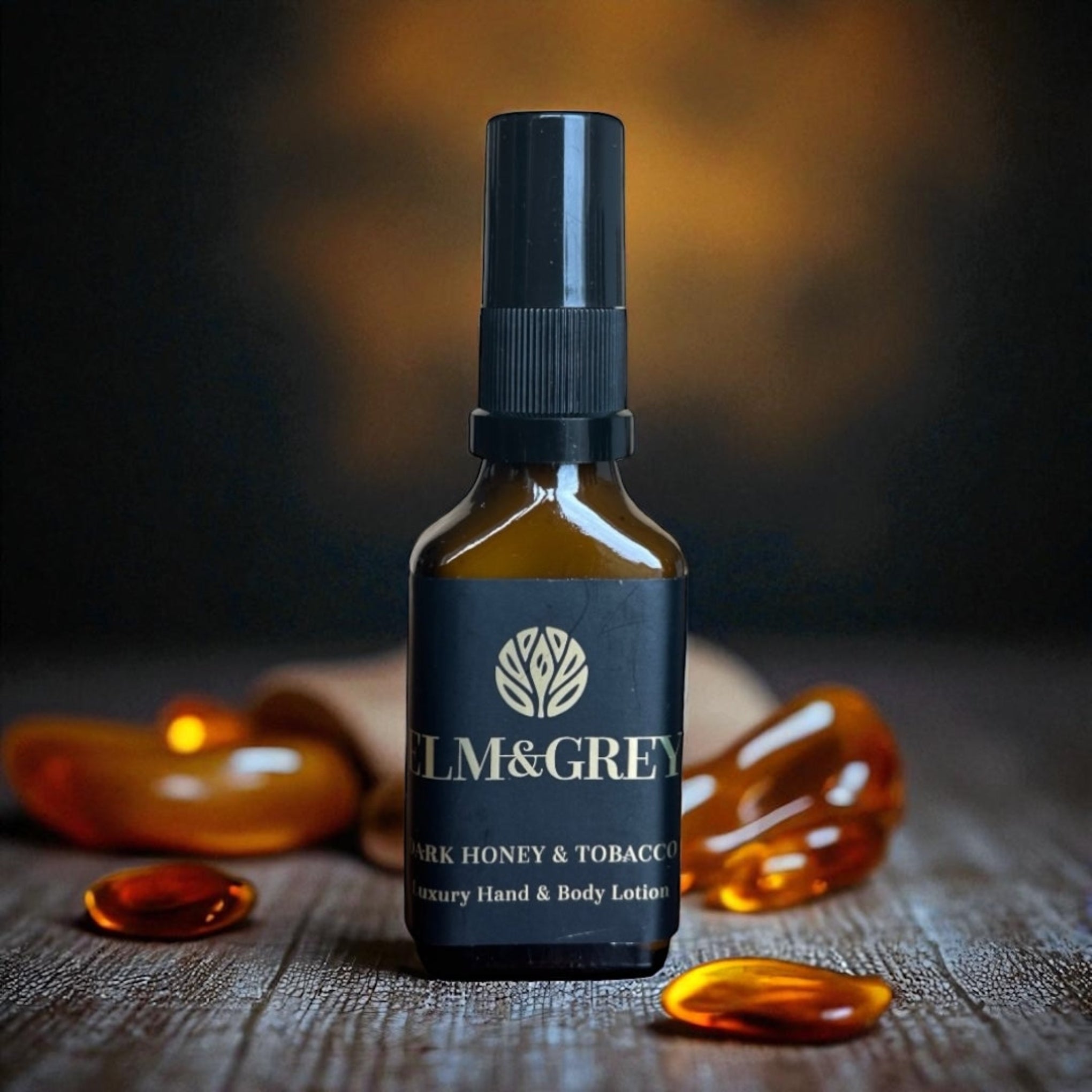 Bottle of Elm & Grey dark honey and tobacco lotion on a wooden surface with blurred background