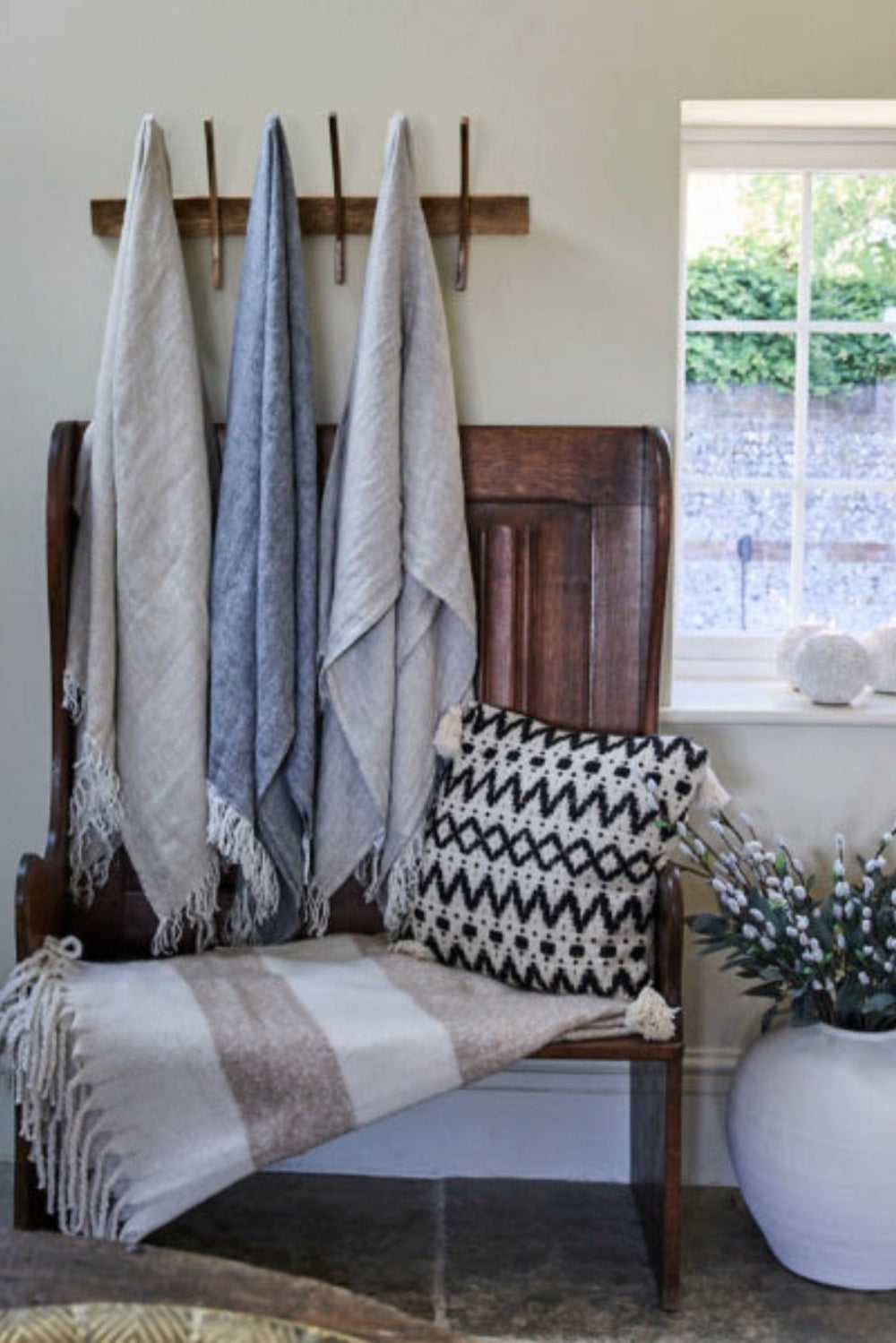 Blankets hanging from hooks a cushion on the seat and a concrete vase on a window sill