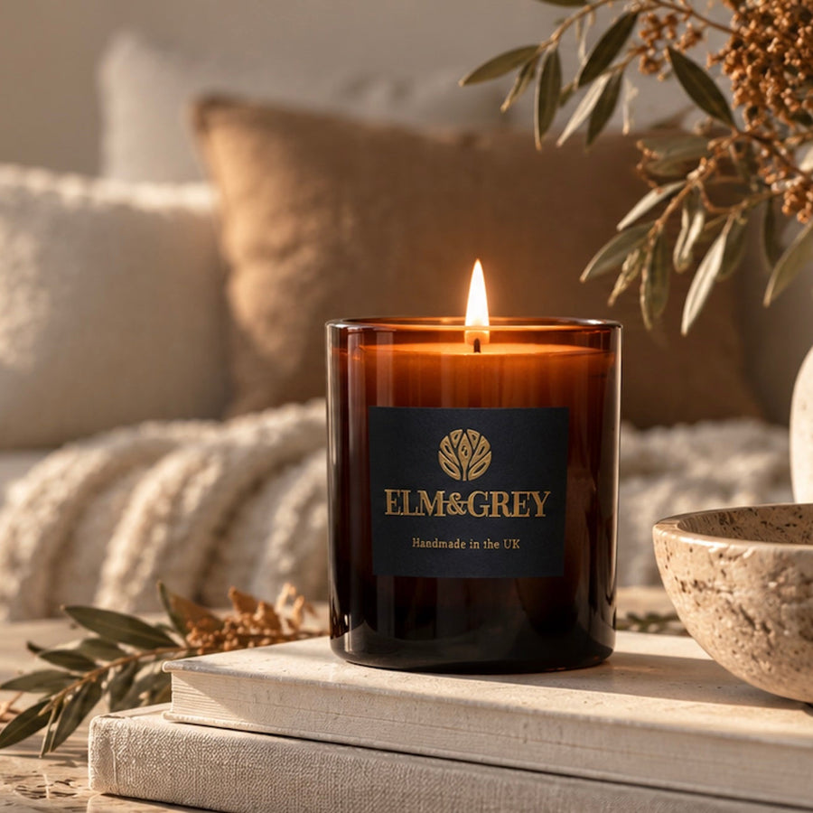 Elm & Grey amber glass candle styled on a neutral coffee table with autumn foliage, stone accessories and soft warm light