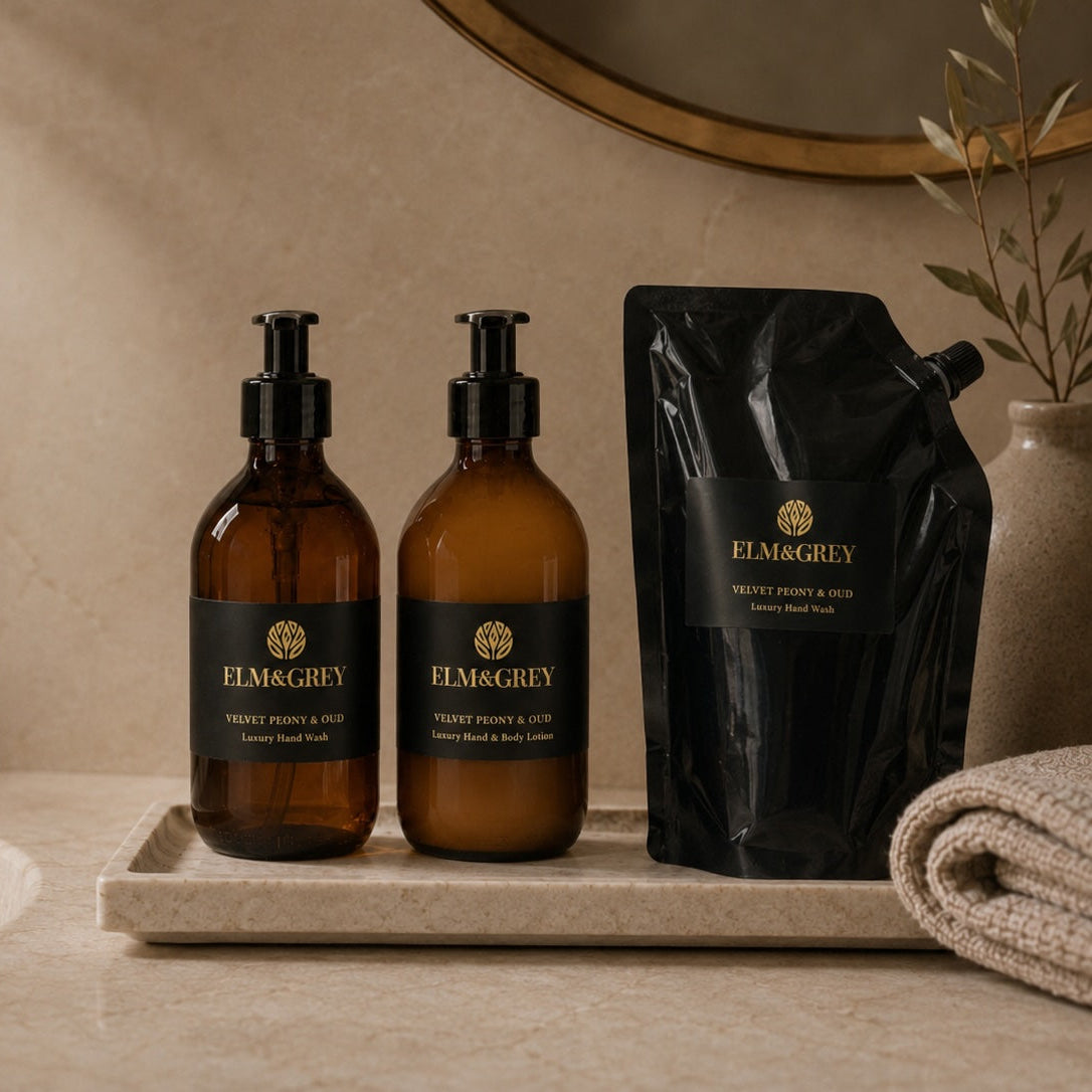 Two amber bottles and a black  refill pouch labeled 'Elm & Grey' on a bathroom counter.