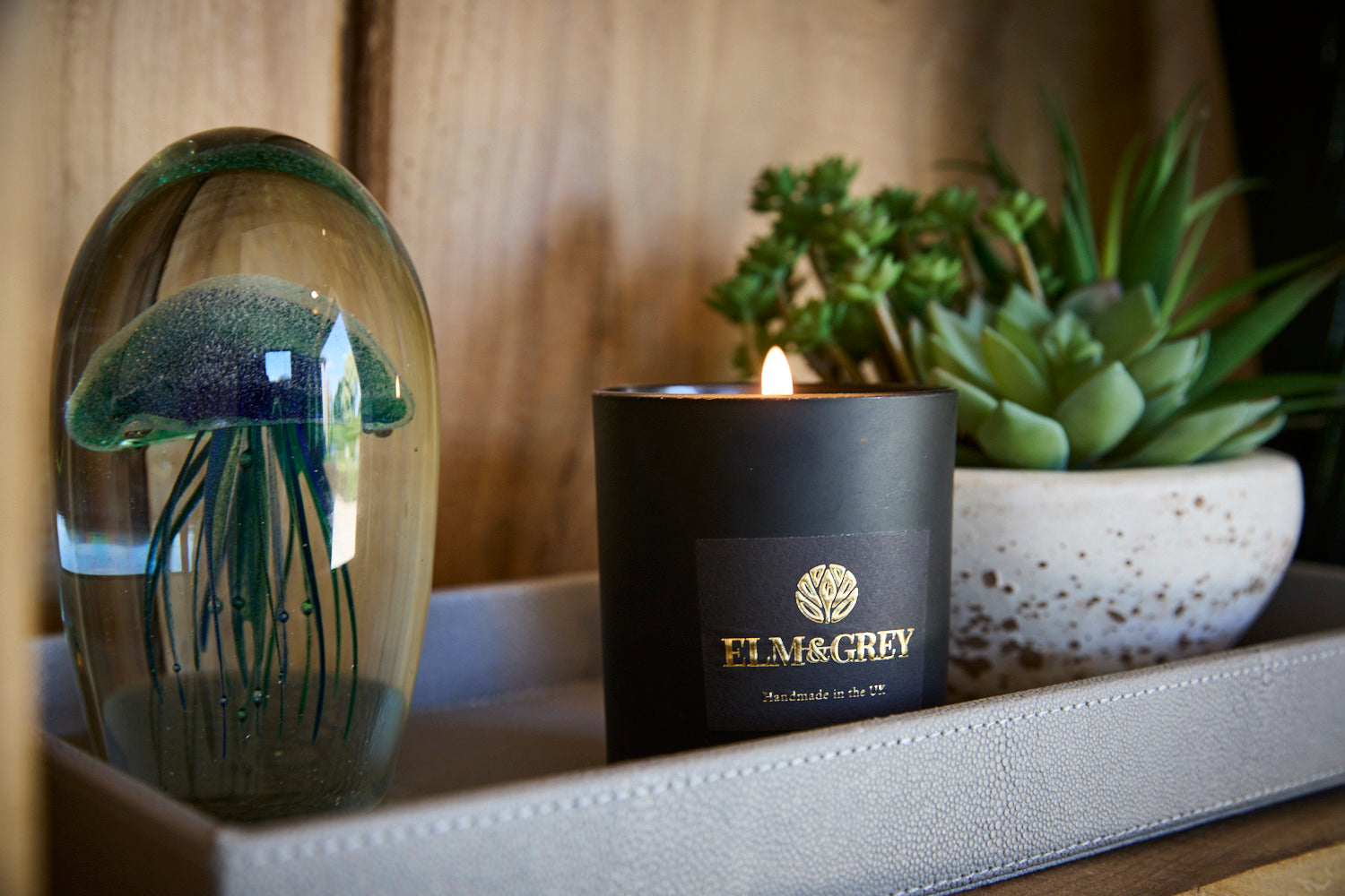 Glass Jellyfish paperweight on a shagreen tray next to a black lit candle and faux succulent